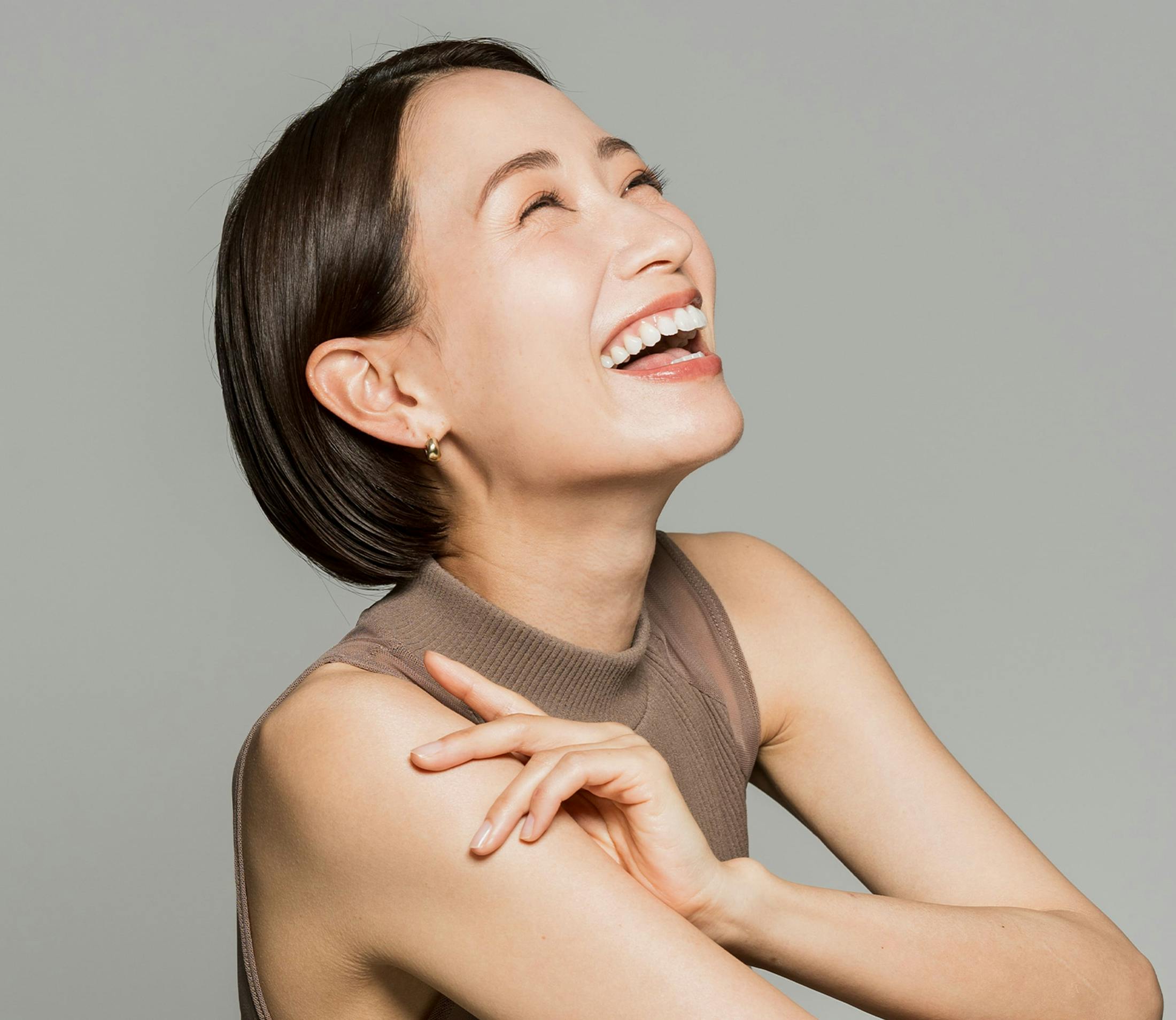 woman laughs while looking upwards in brown tank top