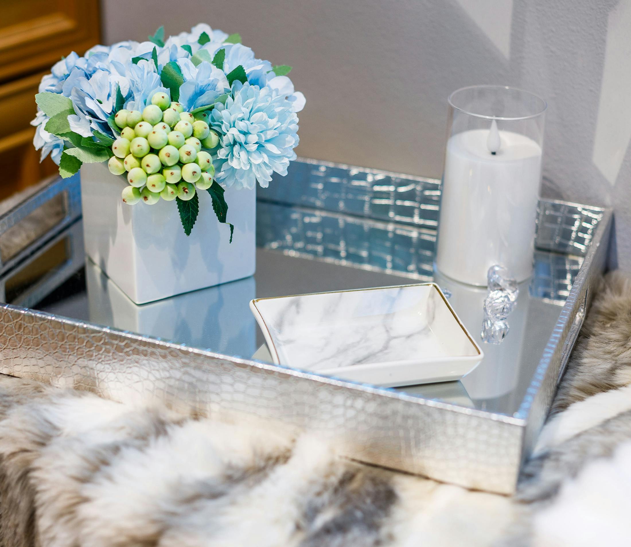 blue and green flowers in a vase on a decorative mirrored tray
