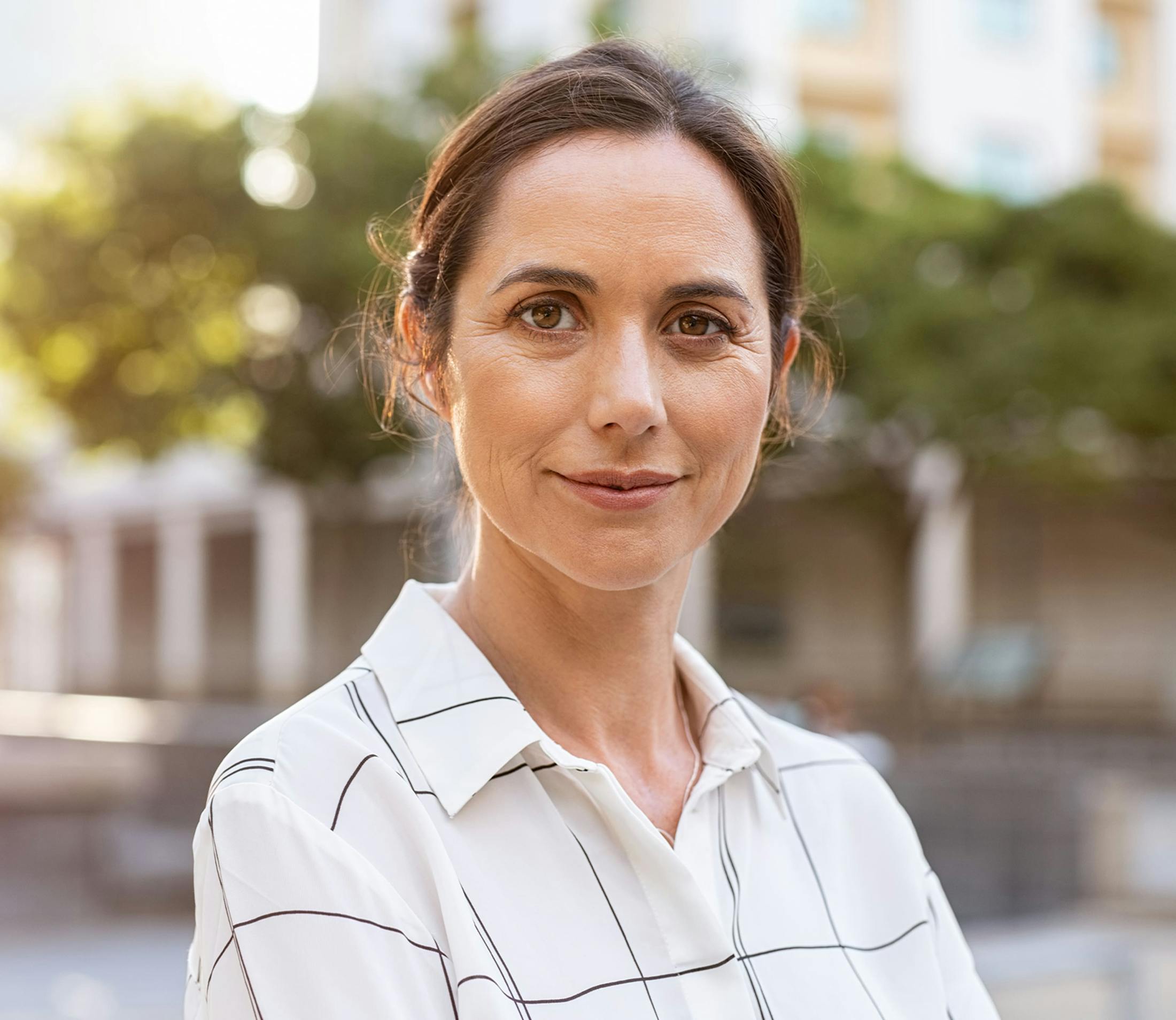 woman in white patterned shirt looking forward with hair in bun
