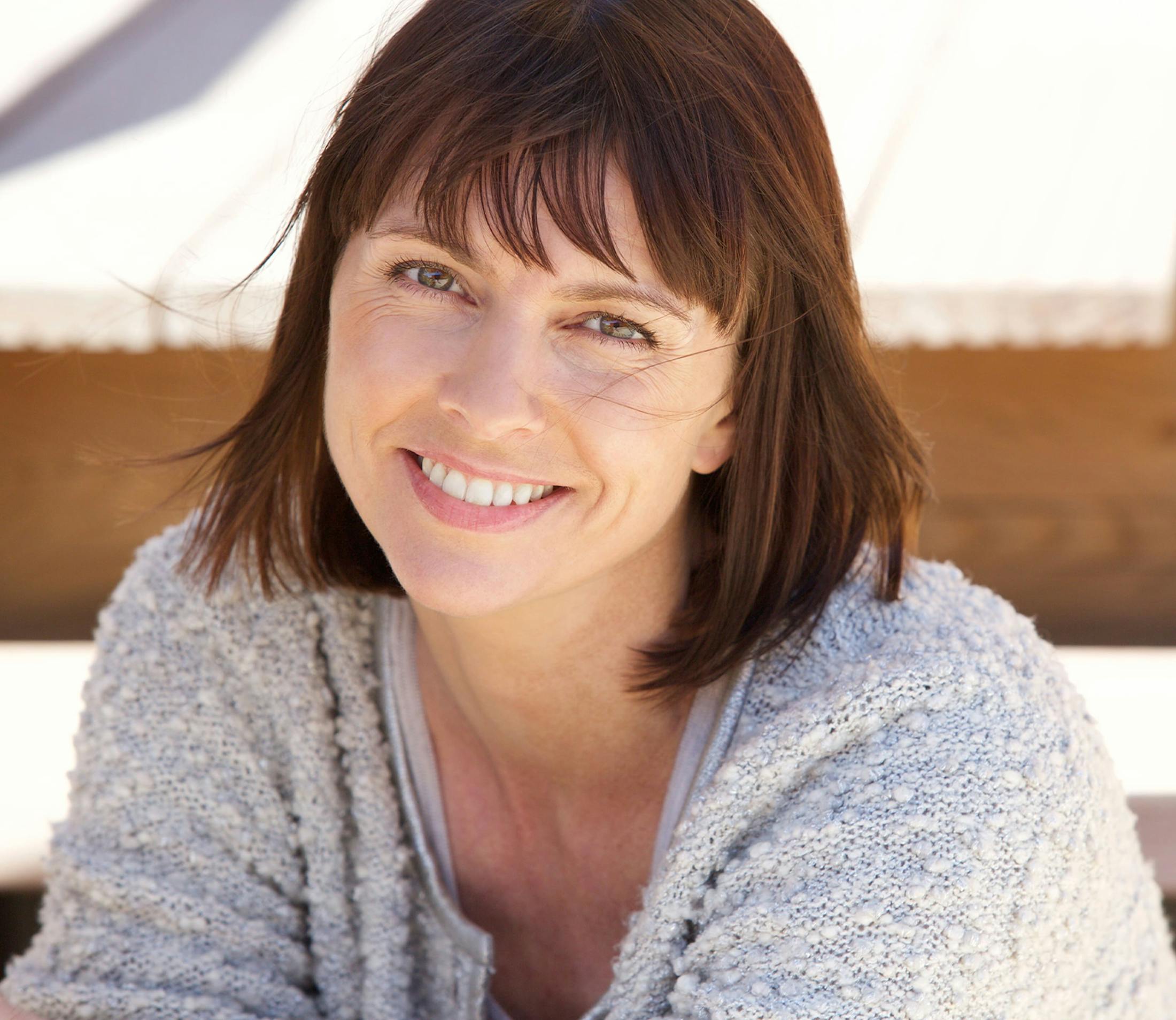 woman in grey sweater smiles while outdoors