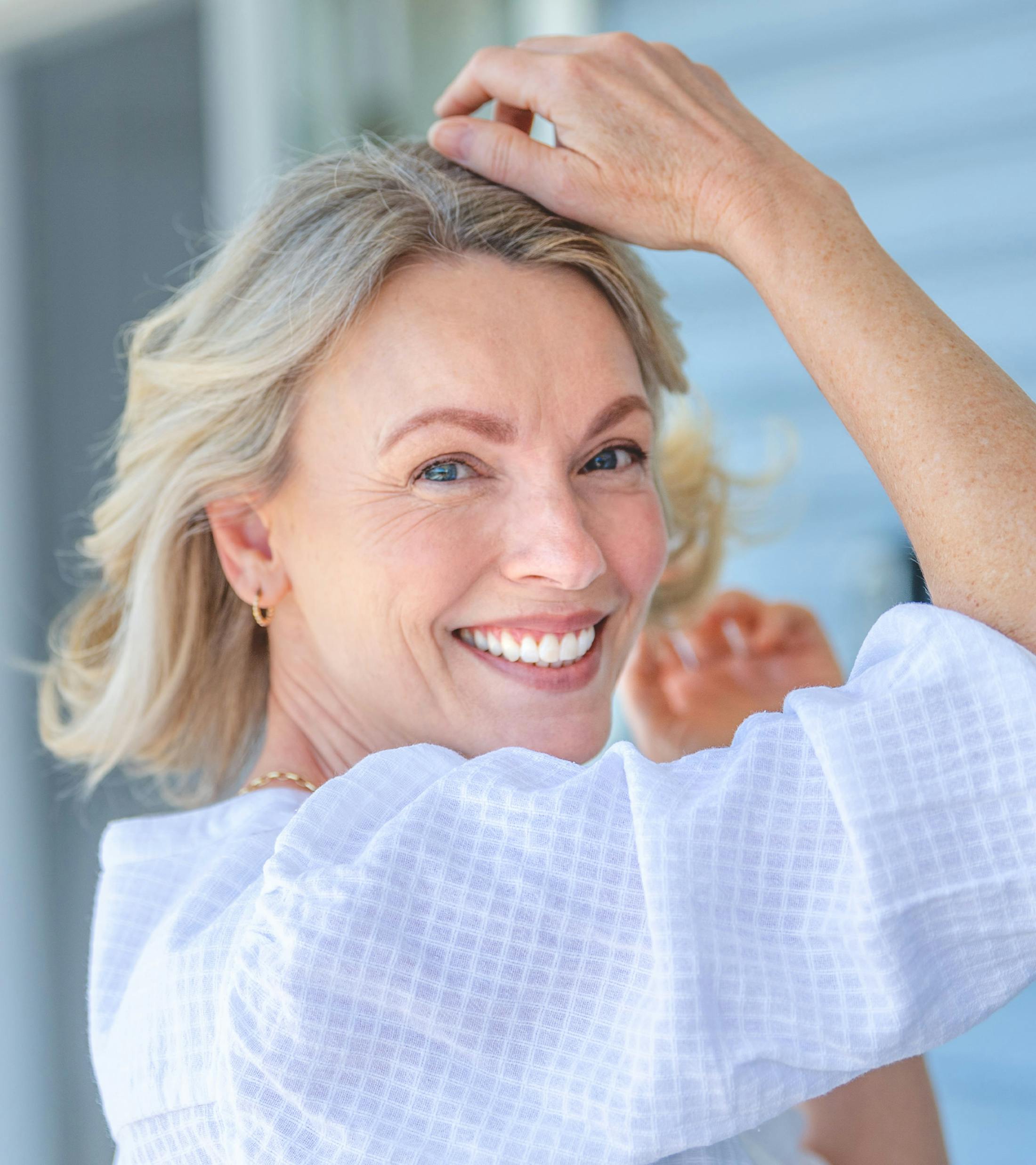 woman in white shirt with her hands above her head, while she looks over her shoulder