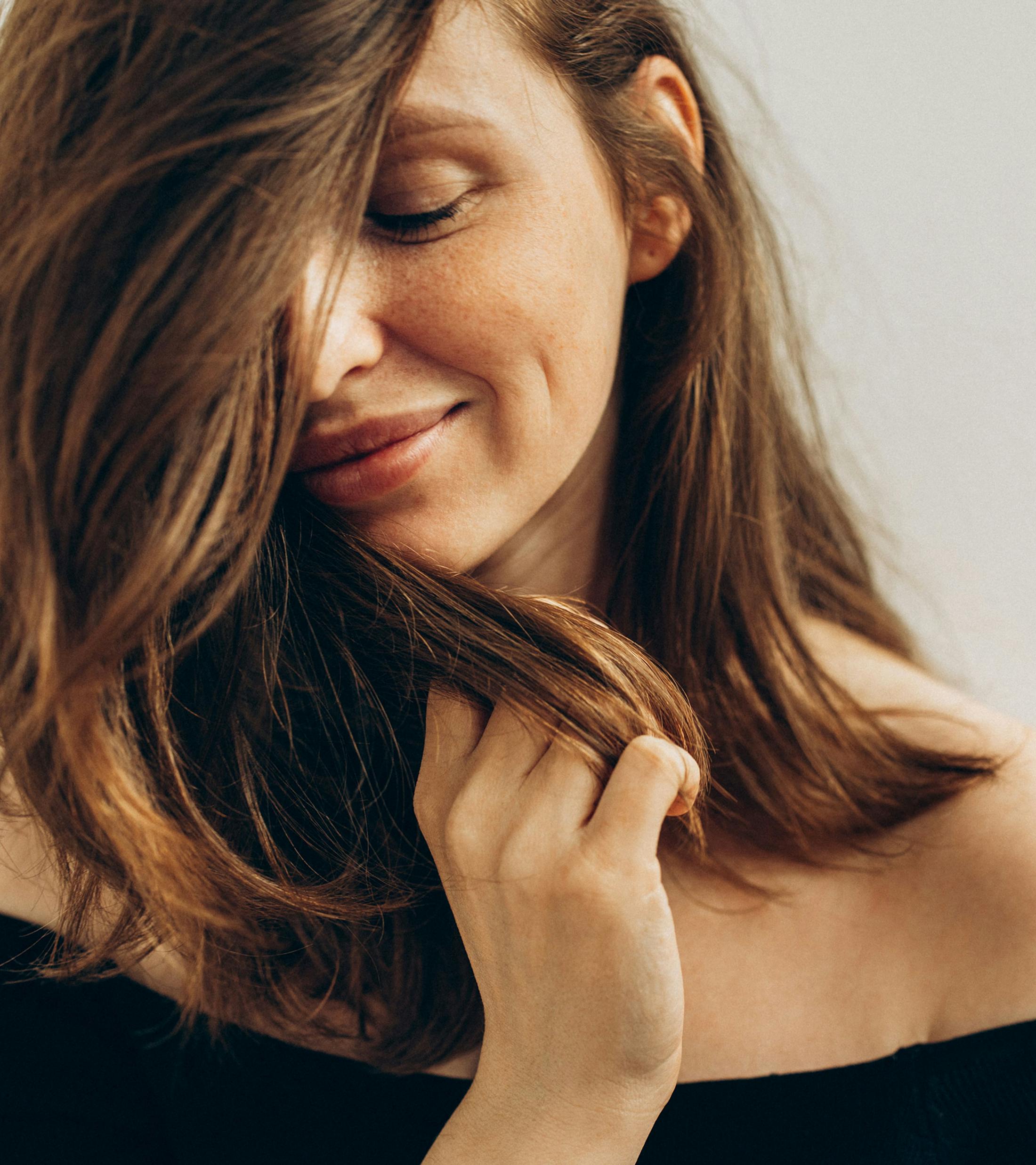 woman with long dark hair, wraps her hair around her face smiling