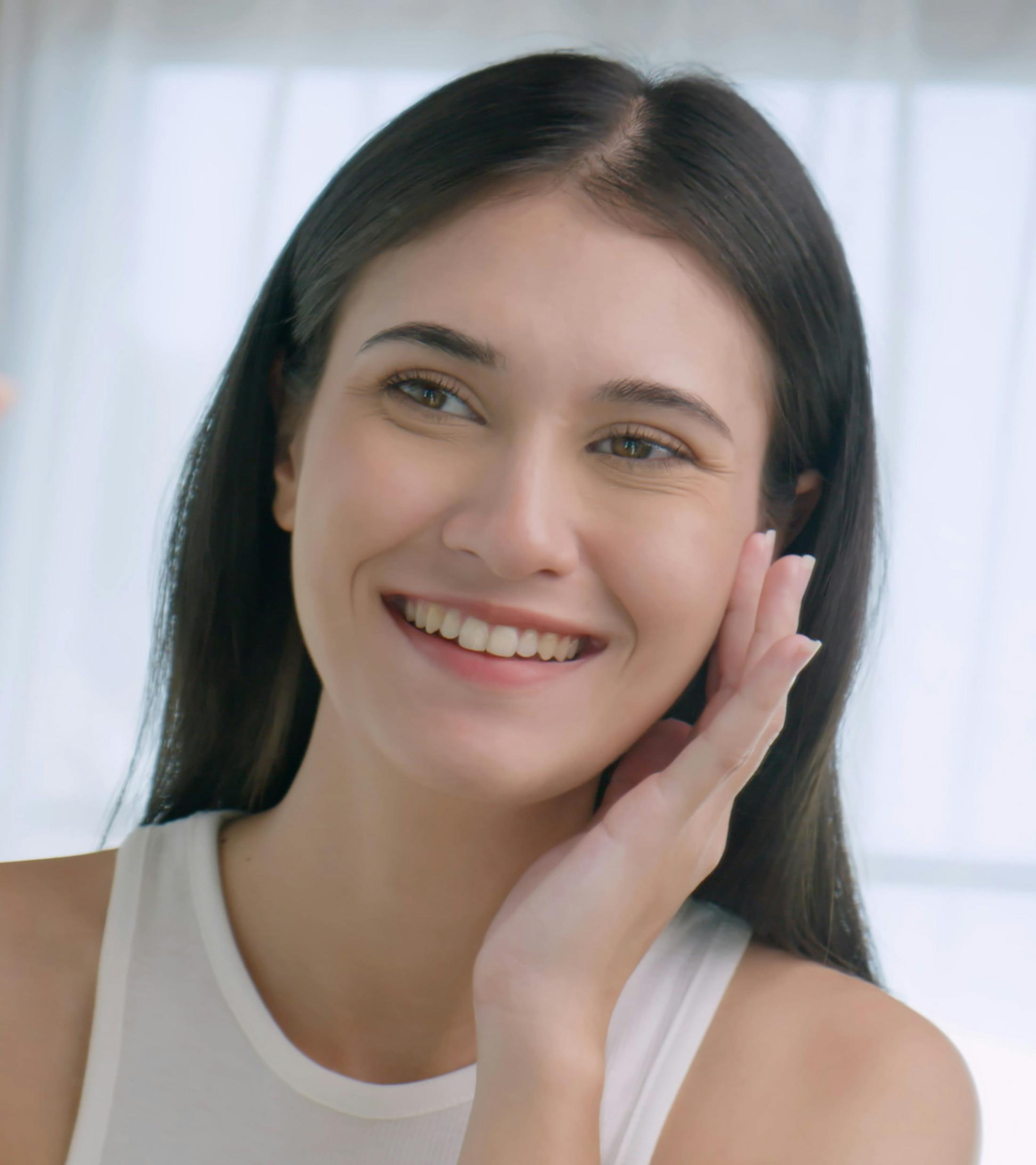 woman in white tank touching her cheek, smiling