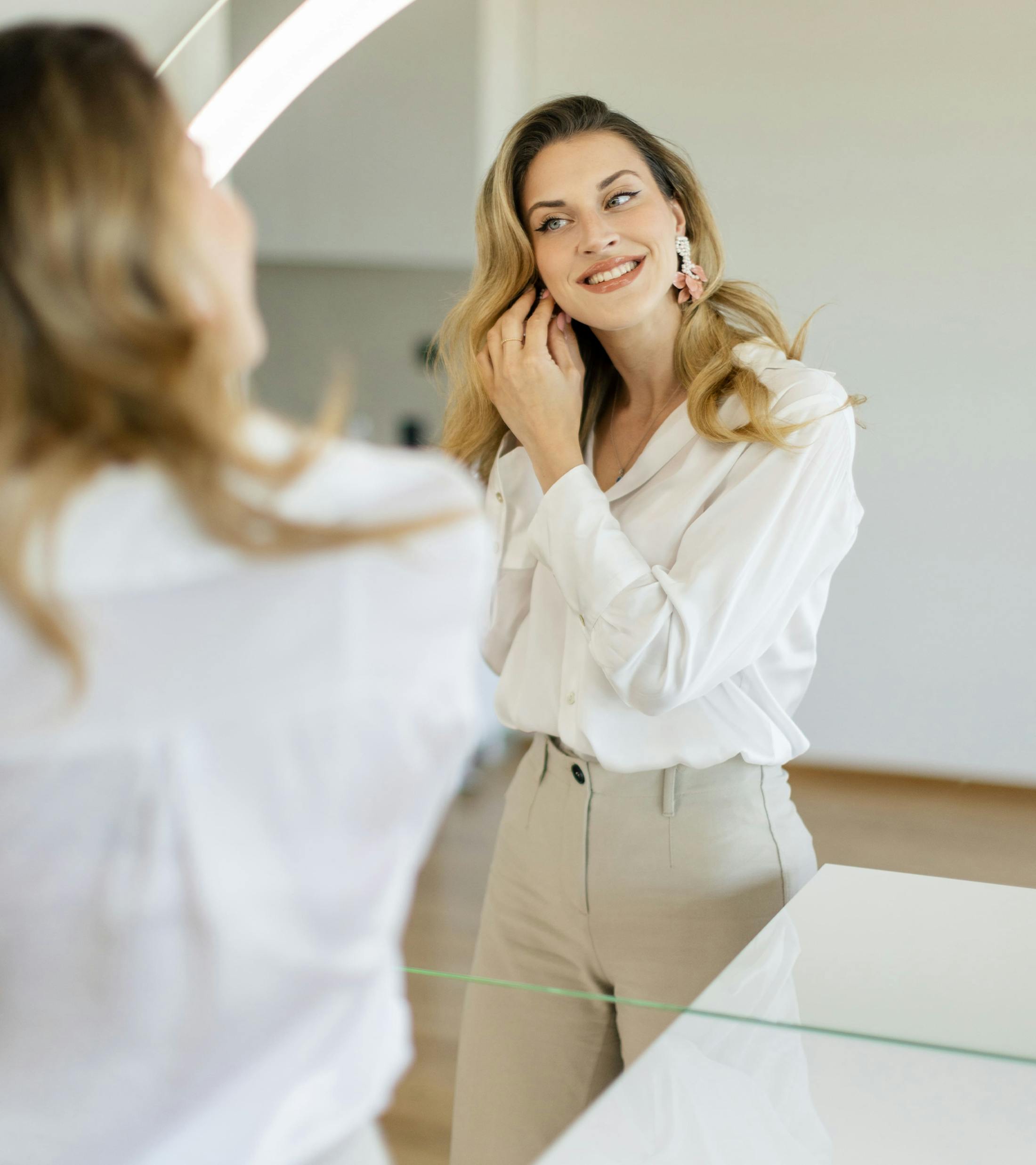 woman looking into mirror while putting on an earring