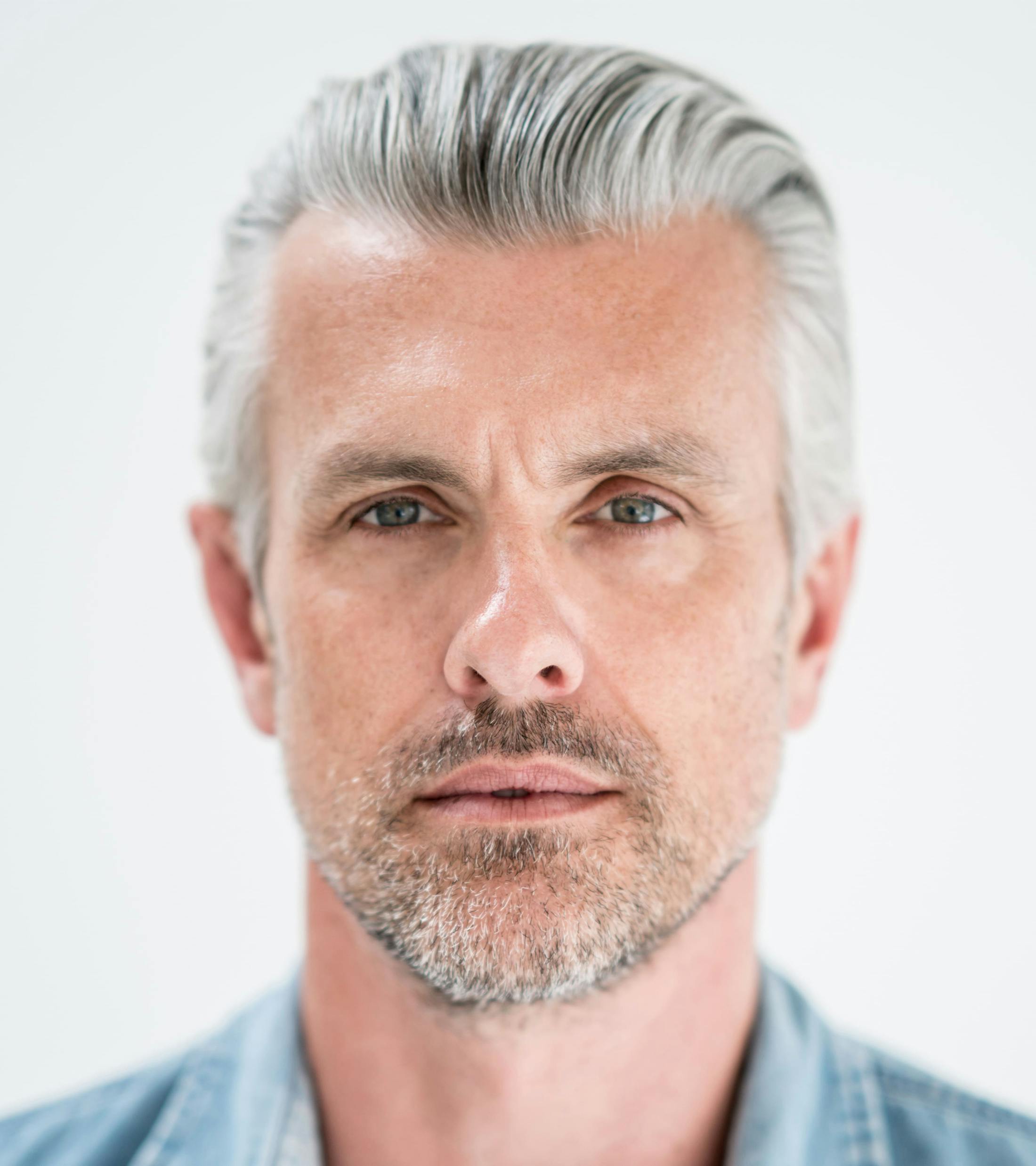 man with grey hair brushed back in blue denim shirt