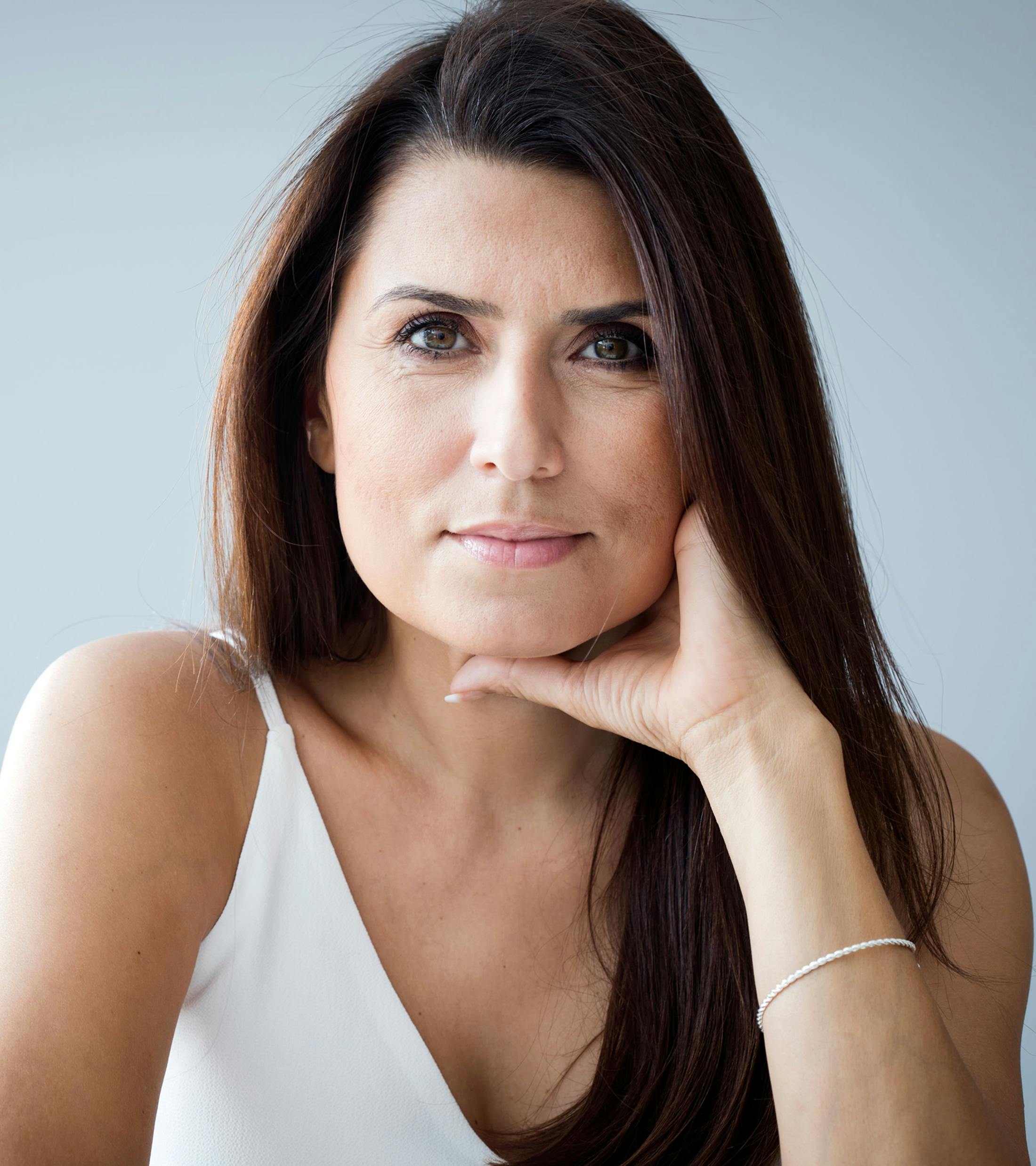 woman with long dark hair looking forward with hand resting on jaw