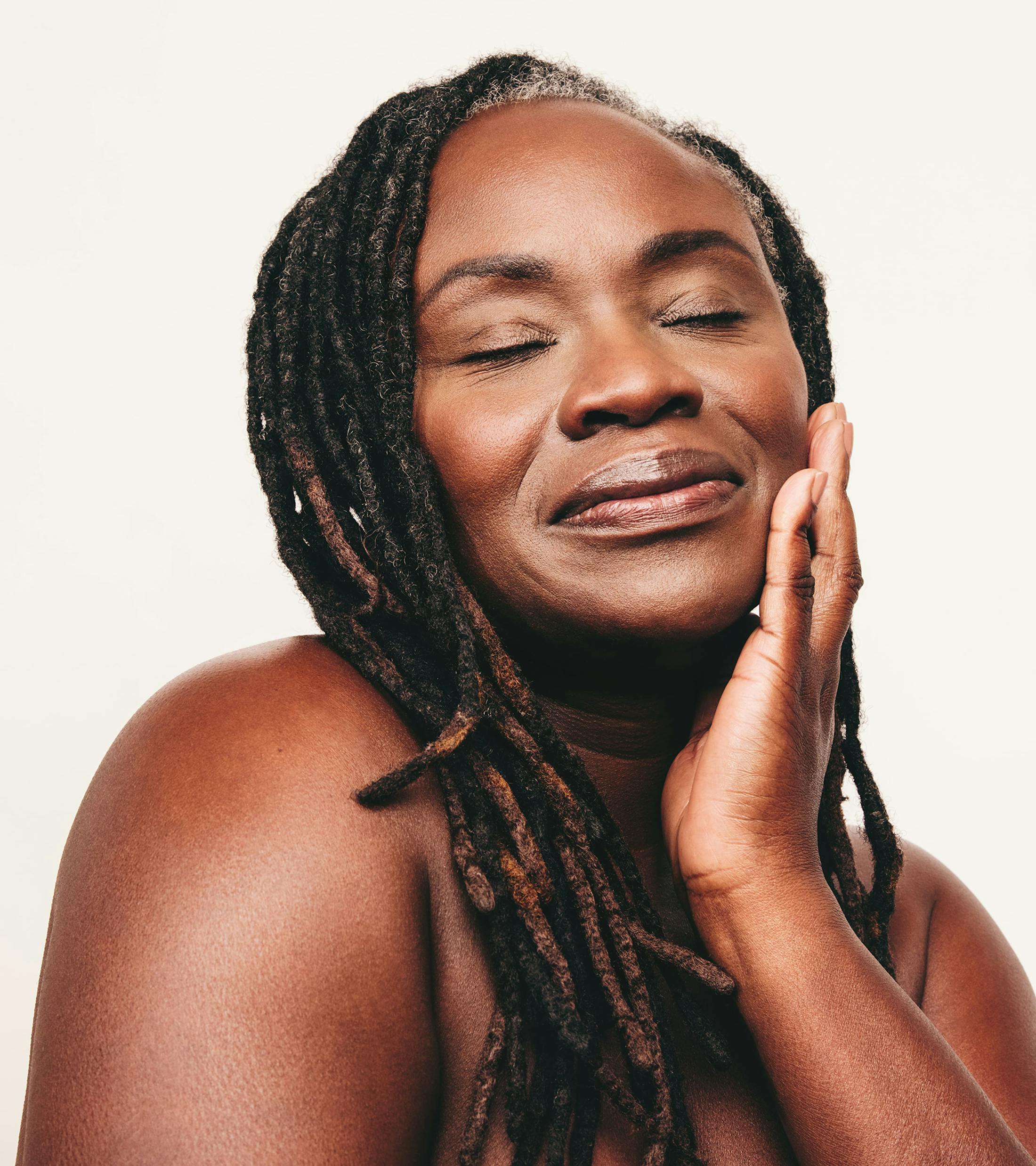 woman with dreads touches her jaw with her eyes closed