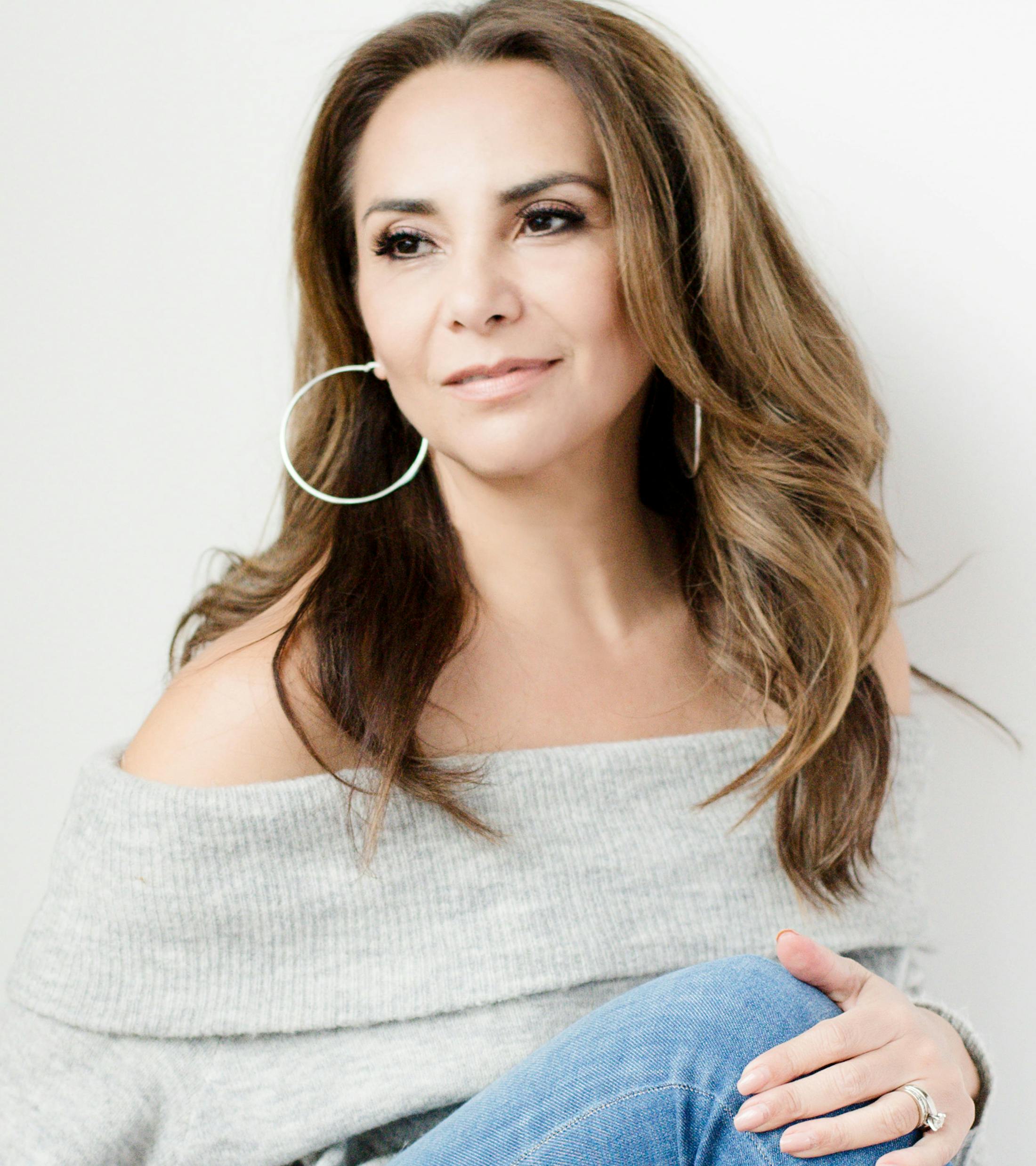 woman in grey sweater, jeans, and large hoop earrings