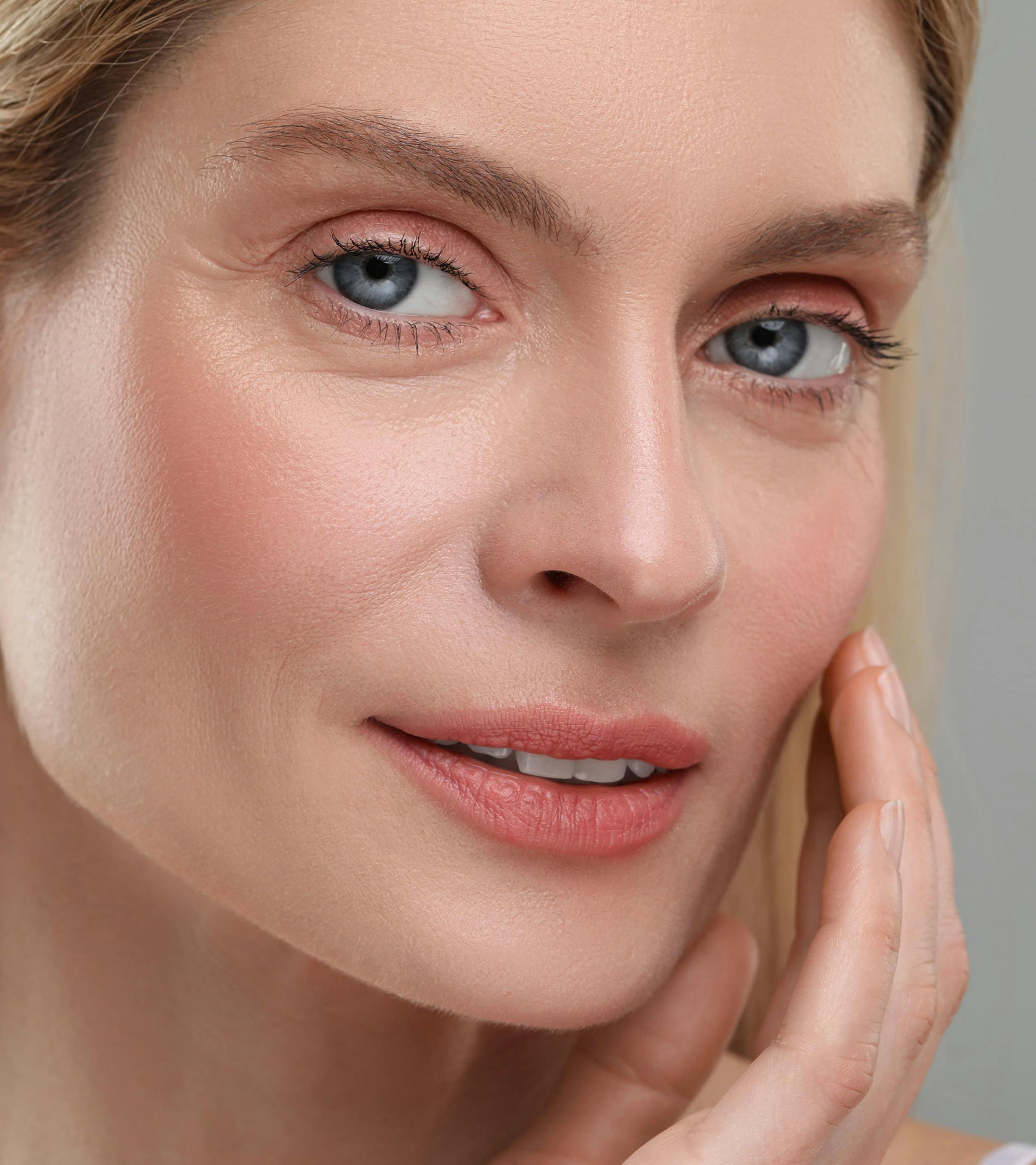 blonde woman touches her cheekbone