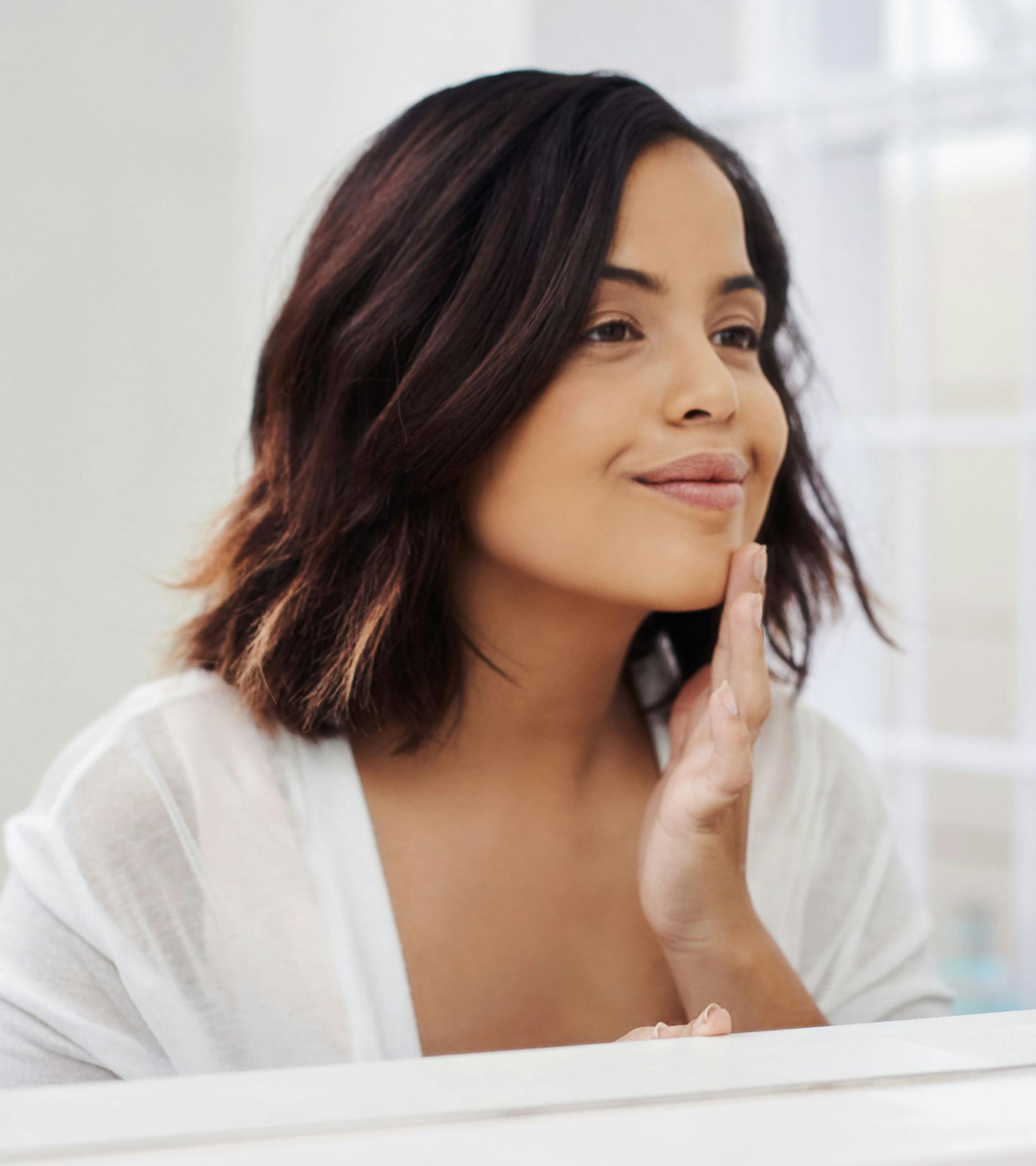 woman looking at herself in the mirror and touching her chin