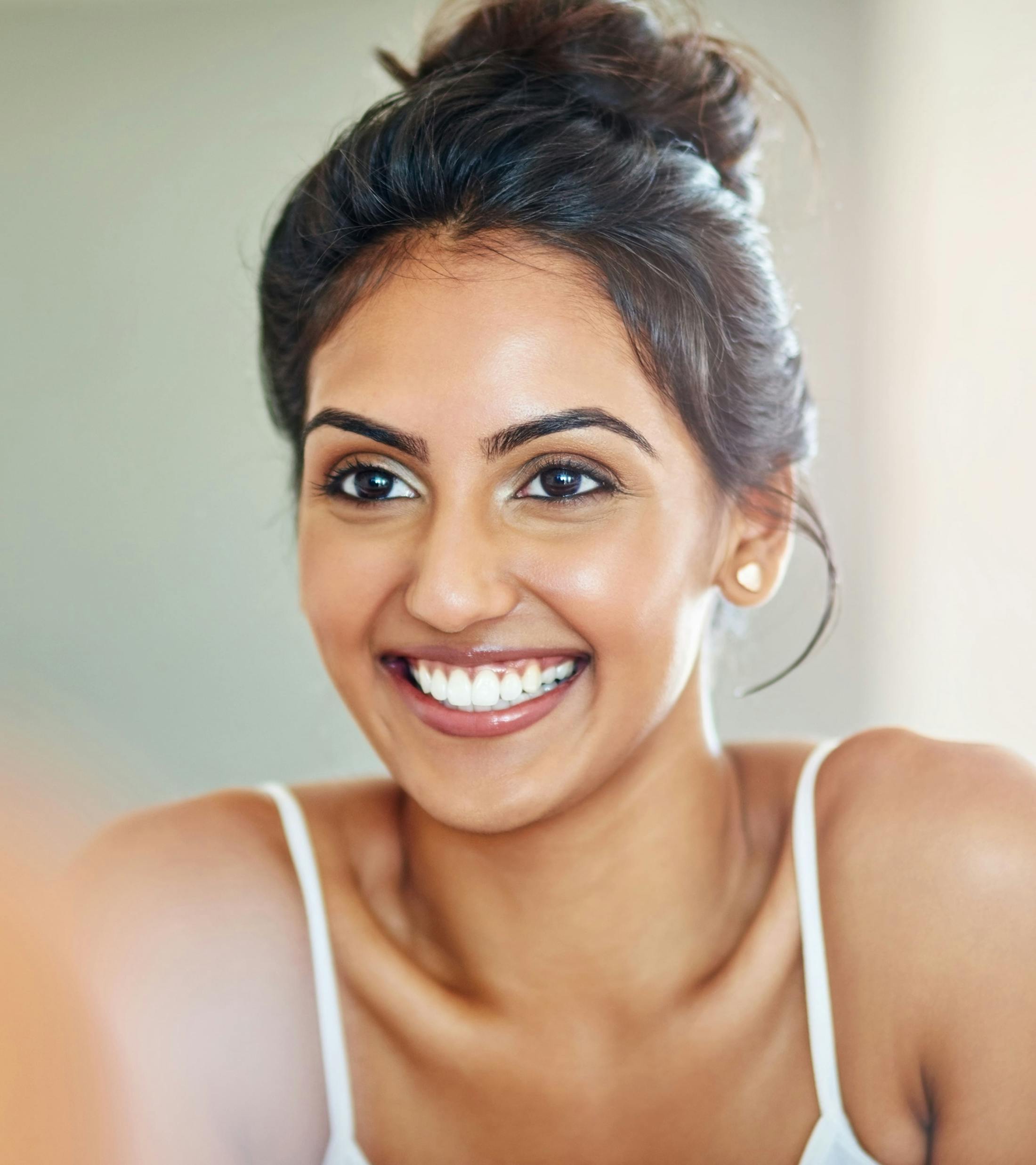 woman with hair in top bun smiles in white camisole