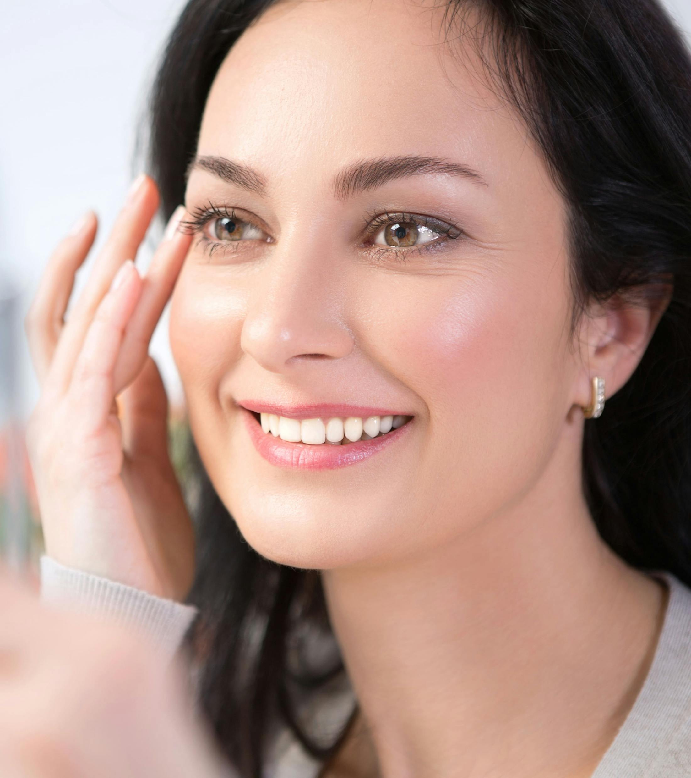 woman touches her temple with her fingers while smiling
