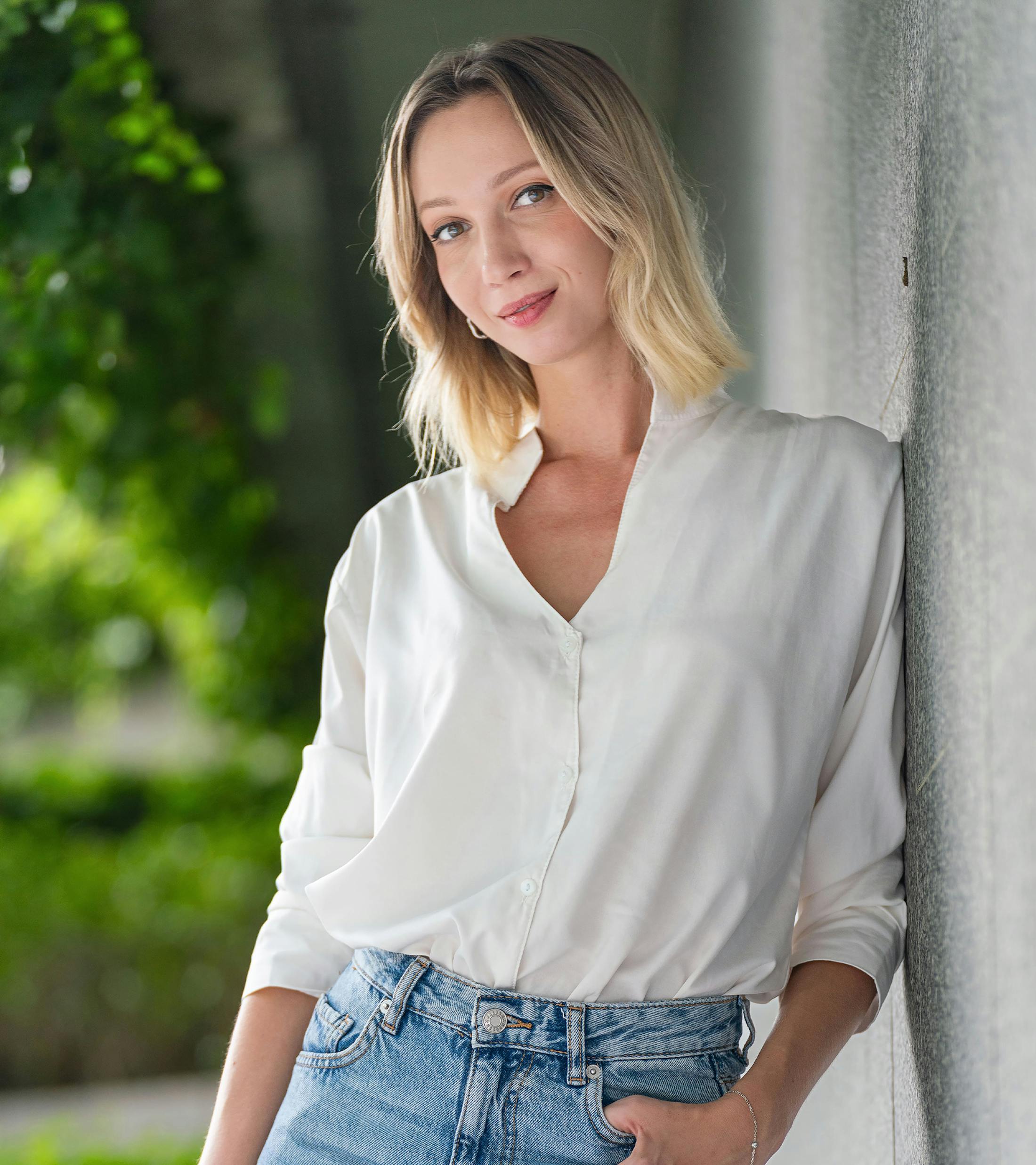 woman standing against cement wall wearing white shirt and jeans