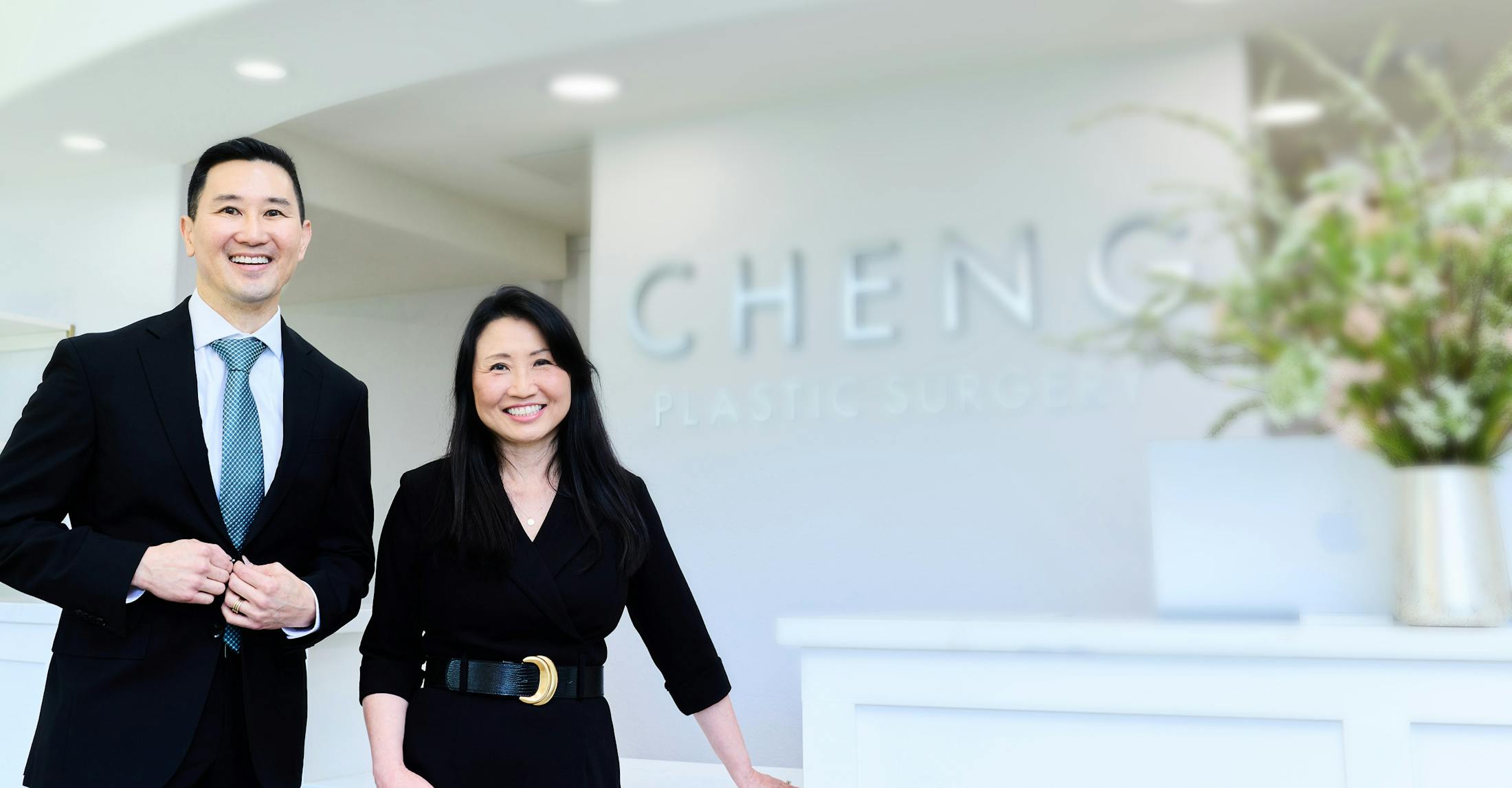 Dr. Elbert Cheng and Dr. Jacqueline Cheng smiling in formal attire at the clinic entrance