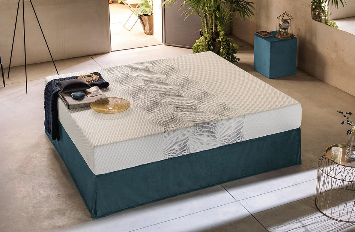 Materasso bianco con decorazione rigata su base blu scuro, coperta e cuscino grigi appoggiati sopra in ambiente moderno con…