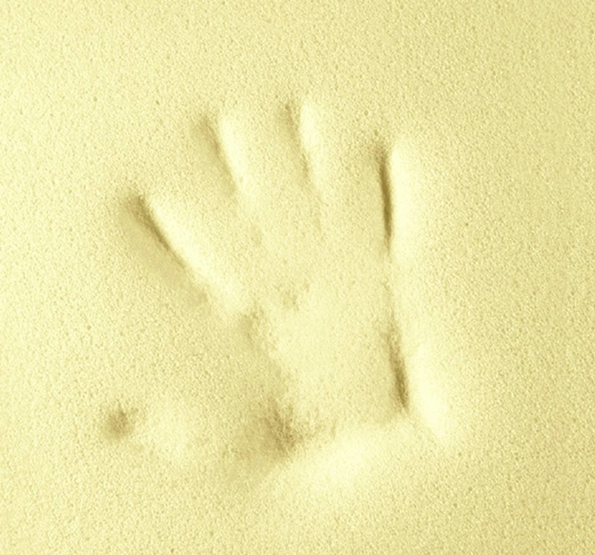 Impronta di mano umana impressa su una superficie morbida e spugnosa di colore giallo chiaro.