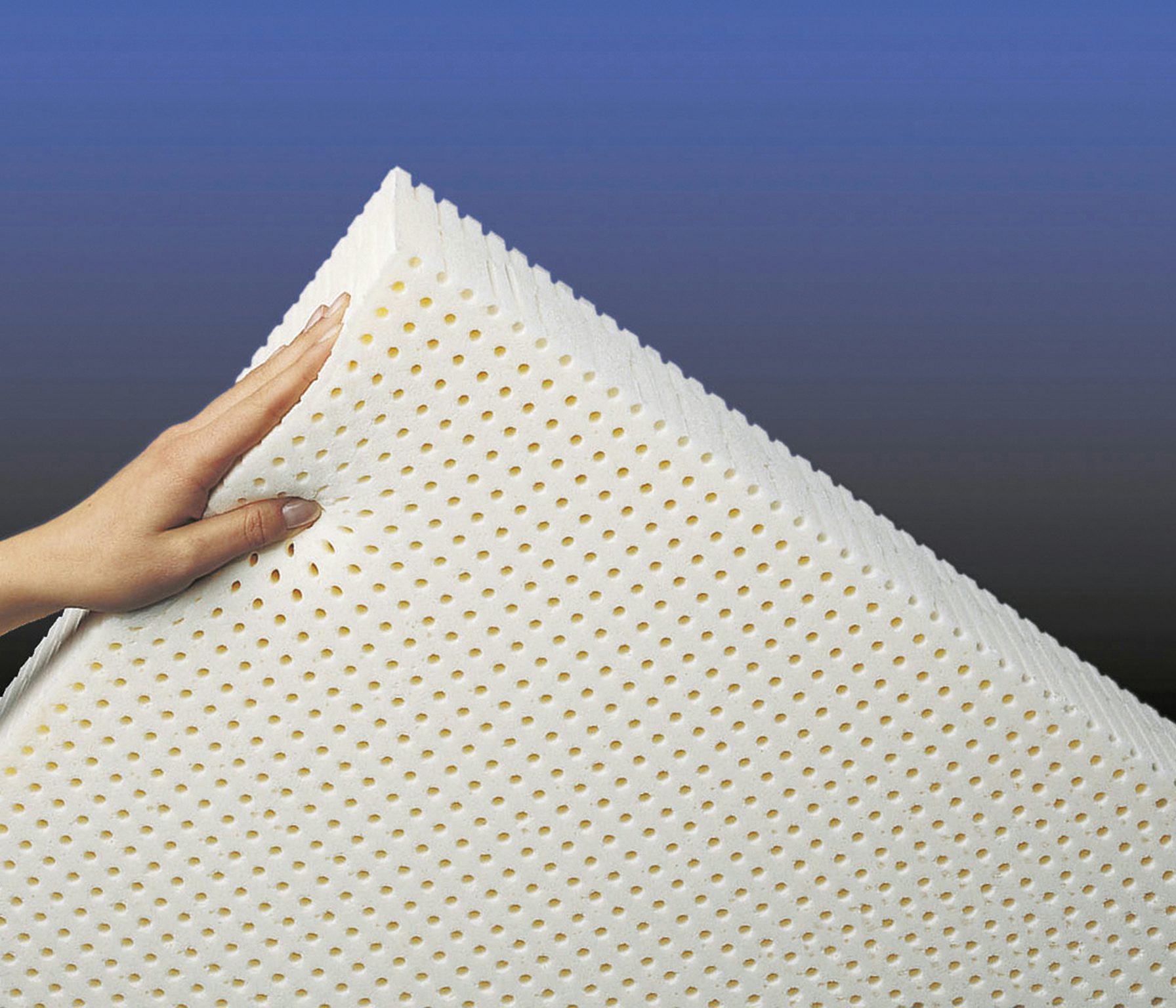 Mano che tiene un materasso o cuscino in lattice bianco con fori per la traspirazione su sfondo sfumato blu.