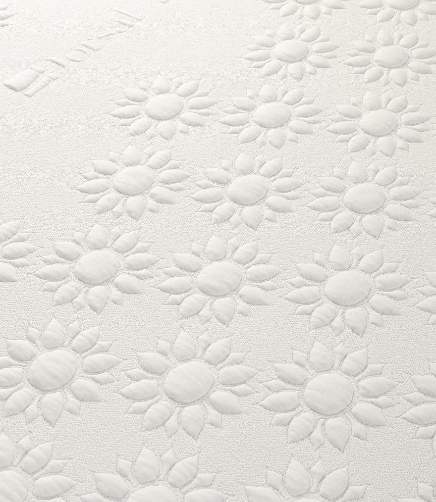 Superficie di materasso bianco con motivo trapuntato a forma di fiori stilizzati e logo parzialmente visibile.