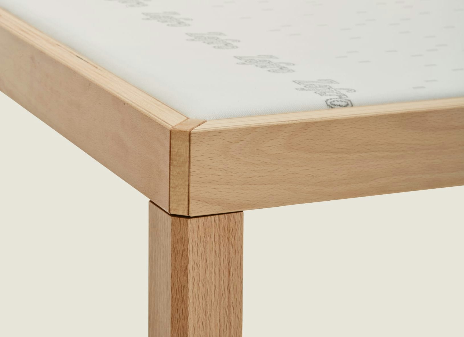 Angolo di un telaio in legno chiaro con gambe squadrate e materasso bianco parzialmente visibile.