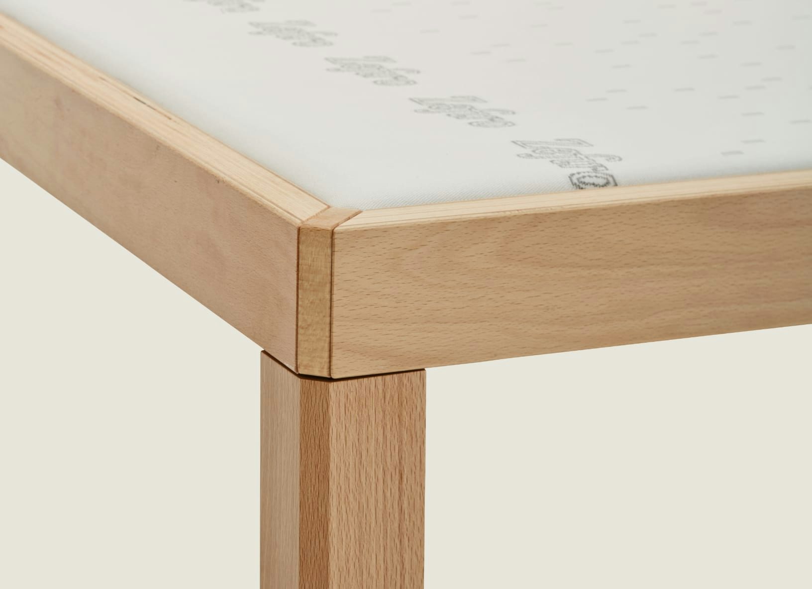 Angolo di un telaio in legno chiaro con gambe squadrate e materasso bianco parzialmente visibile.