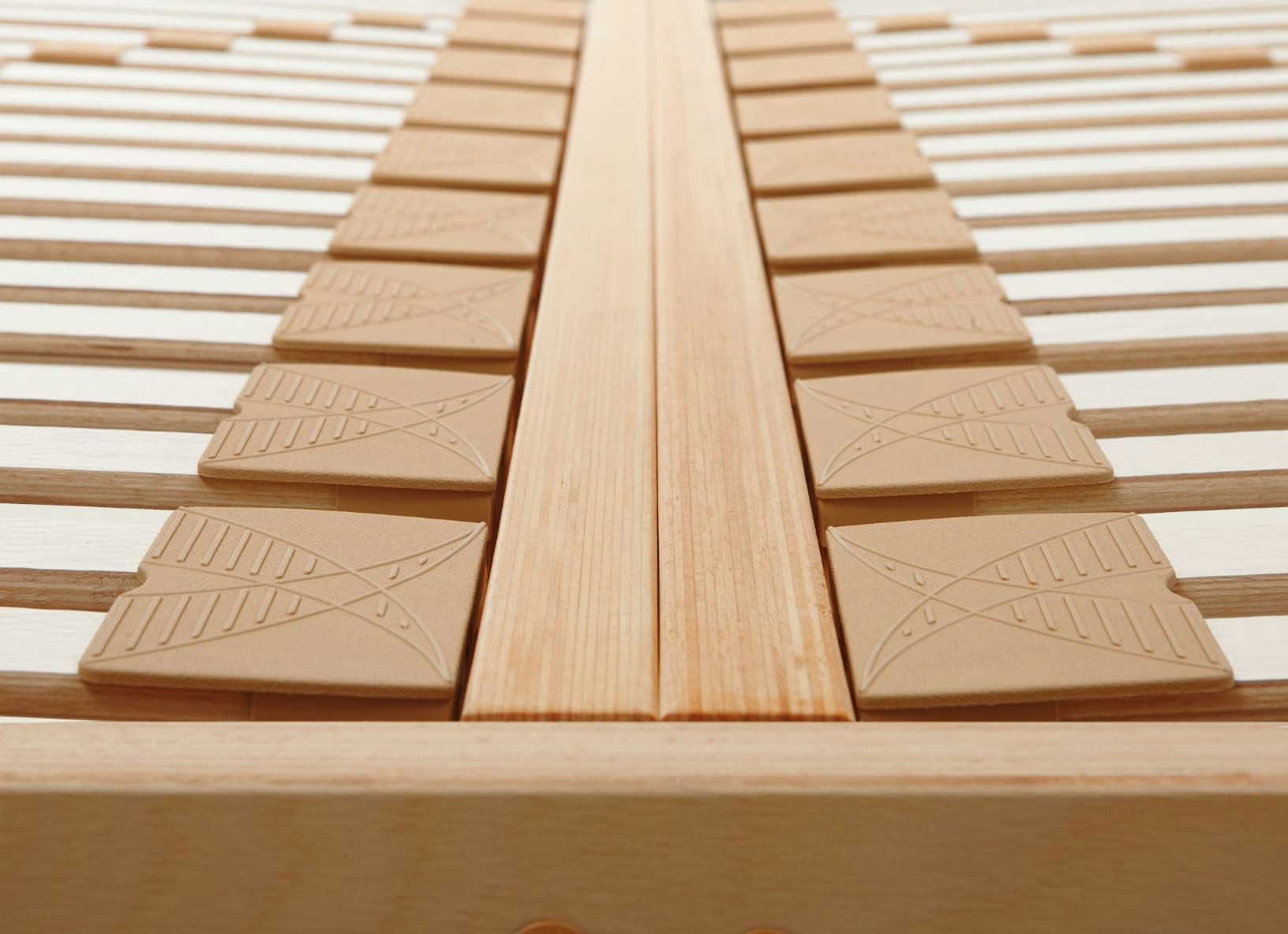 Particolare di struttura letto in legno con supporti in materiale gommoso beige per le doghe.