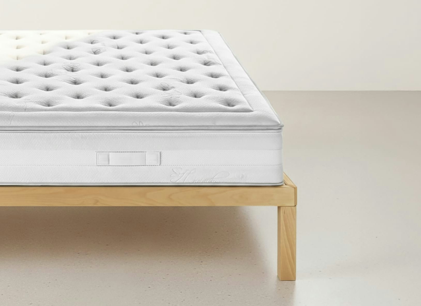 Materasso bianco con imbottitura trapuntata su struttura semplice in legno chiaro su pavimento chiaro.