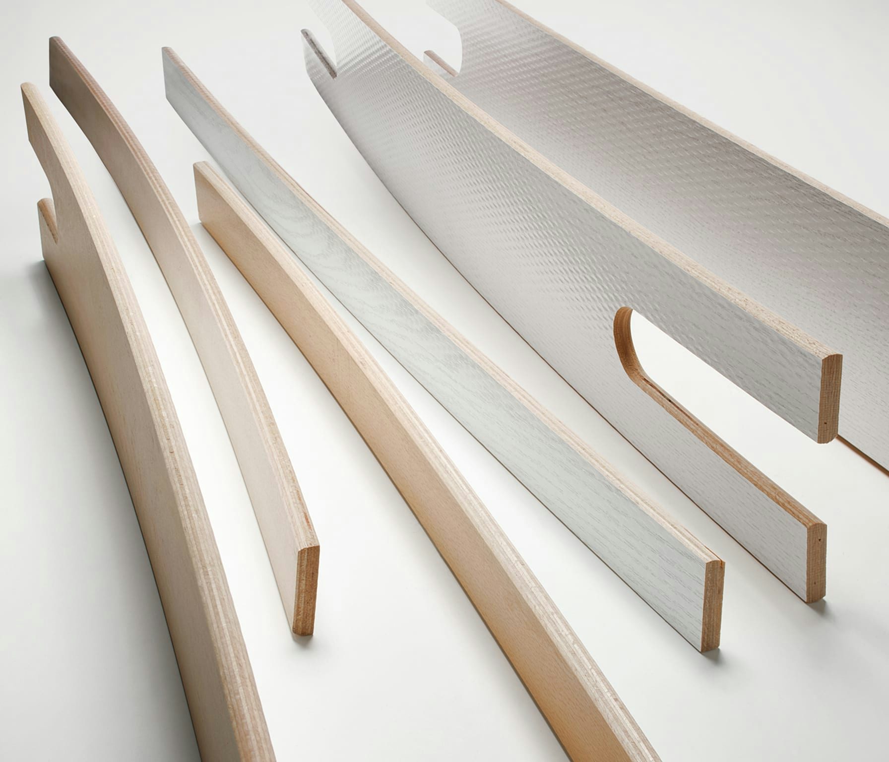 Cinque listelli di legno di varie dimensioni e forme, alcuni con fessure o curve, disposti su sfondo bianco.