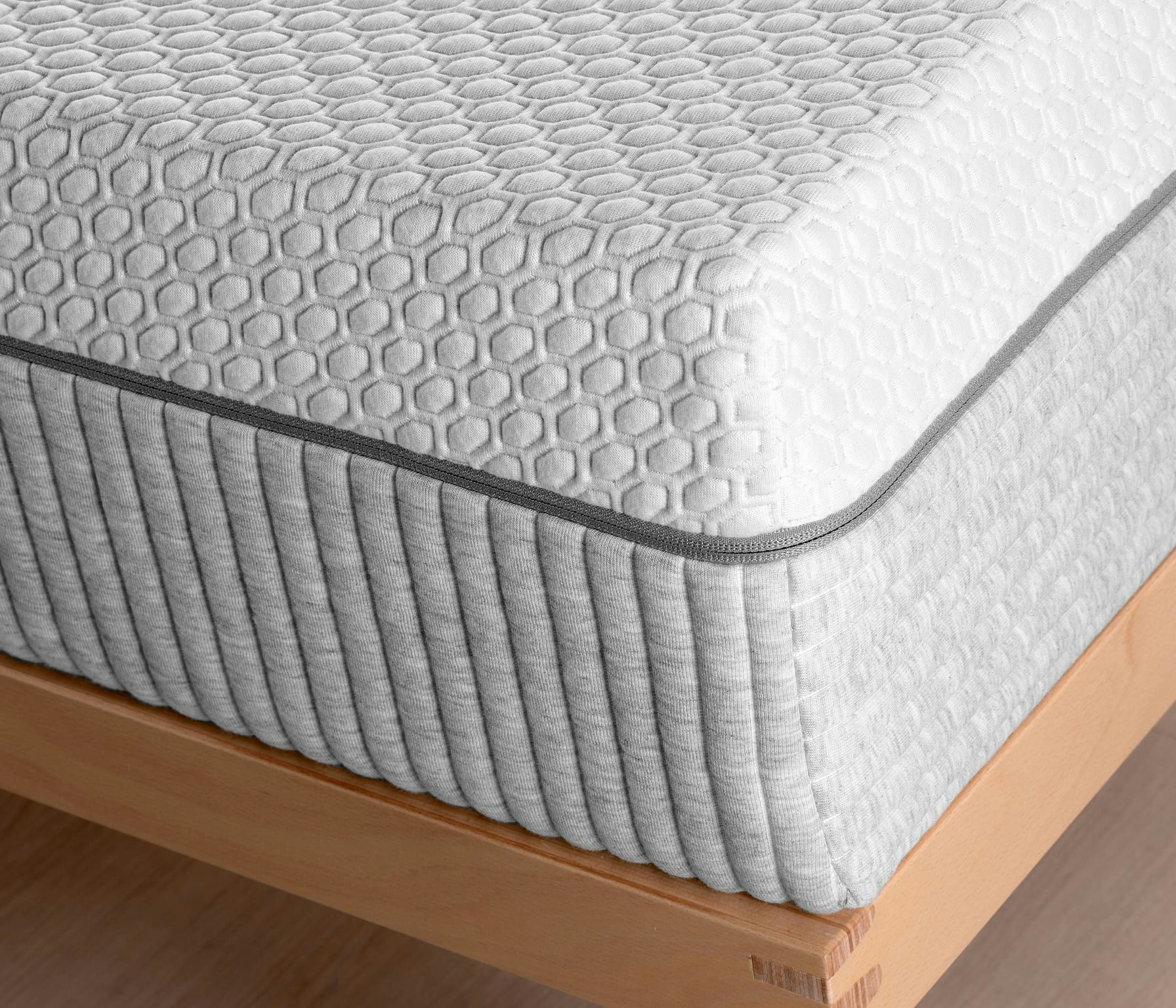 Dettaglio angolo materasso bianco con motivo esagonale e bordi grigi su struttura in legno chiaro.