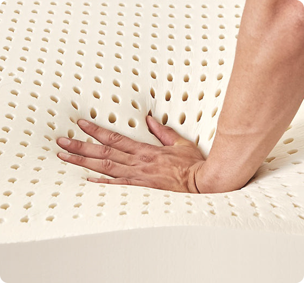 Mano che preme su materasso in schiuma viscoelastica beige con fori traspiranti.