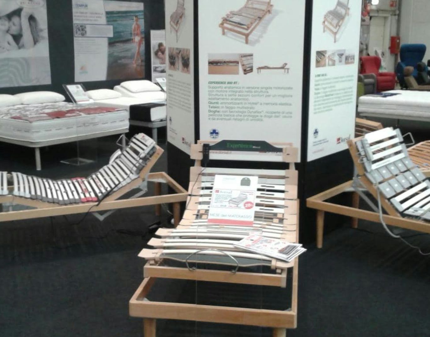 Letti articolati in legno e metallo con rete a doghe esposti in showroom con materassi e cuscini sullo sfondo.