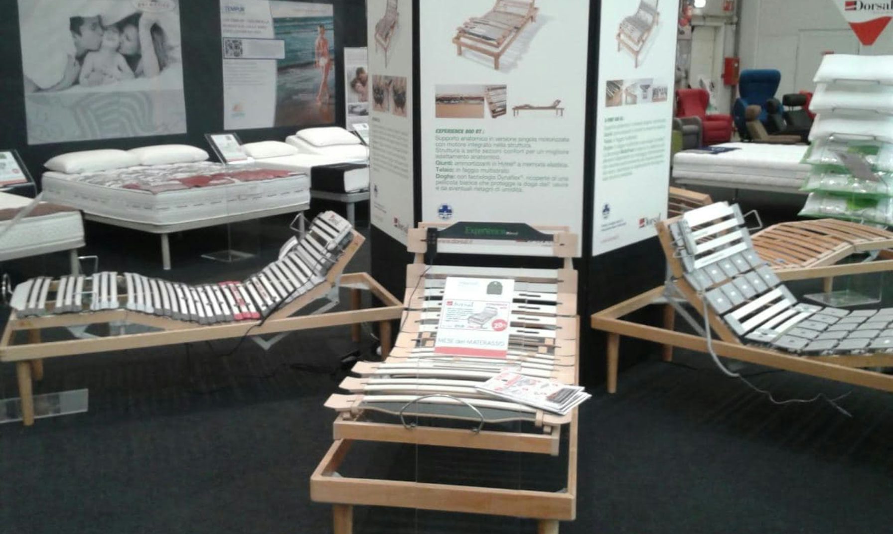 Letti articolati in legno e metallo con rete a doghe esposti in showroom con materassi e cuscini sullo sfondo.