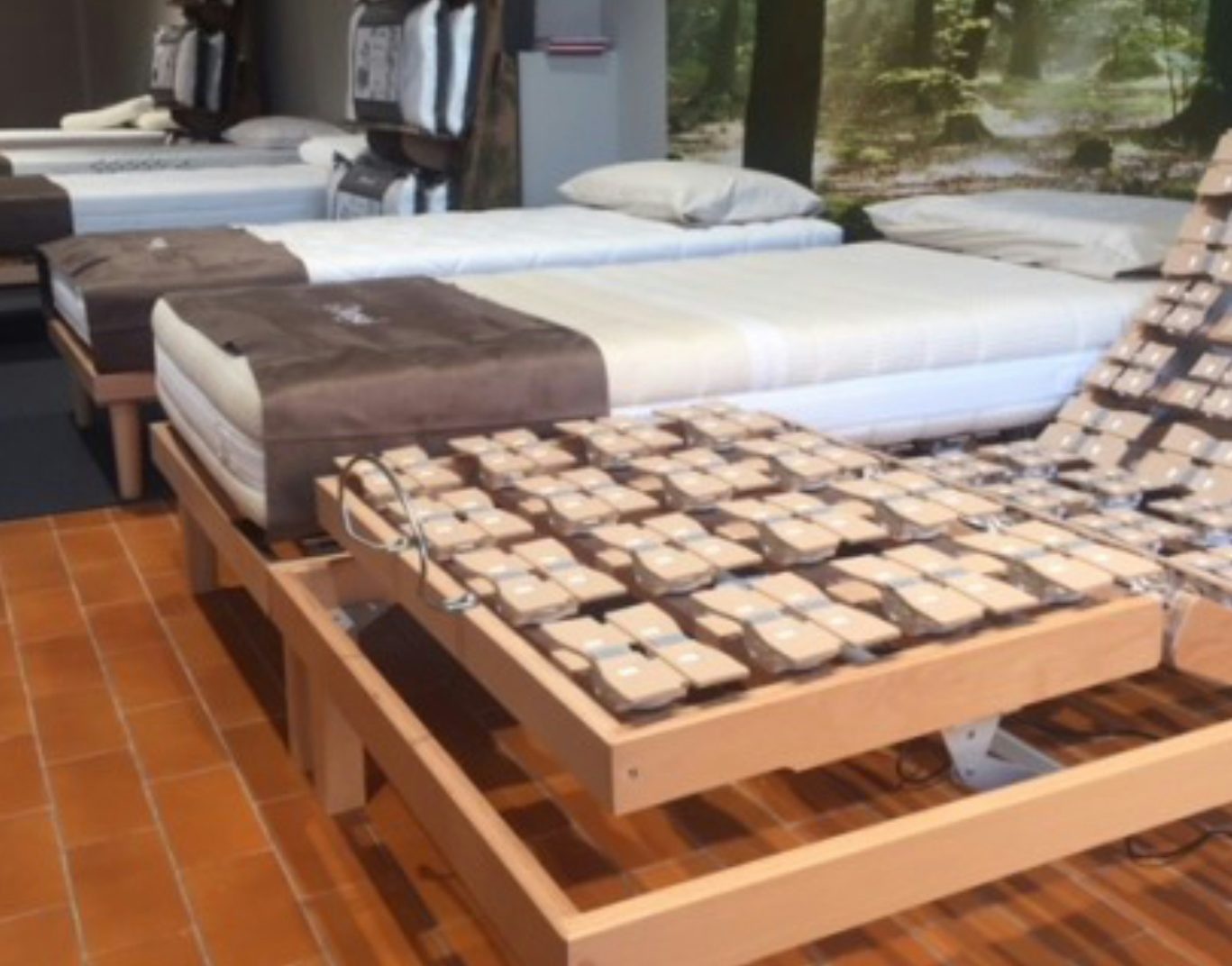 Letti singoli con rete regolabile e materassi in esposizione su pavimento in mattonelle arancioni in showroom.