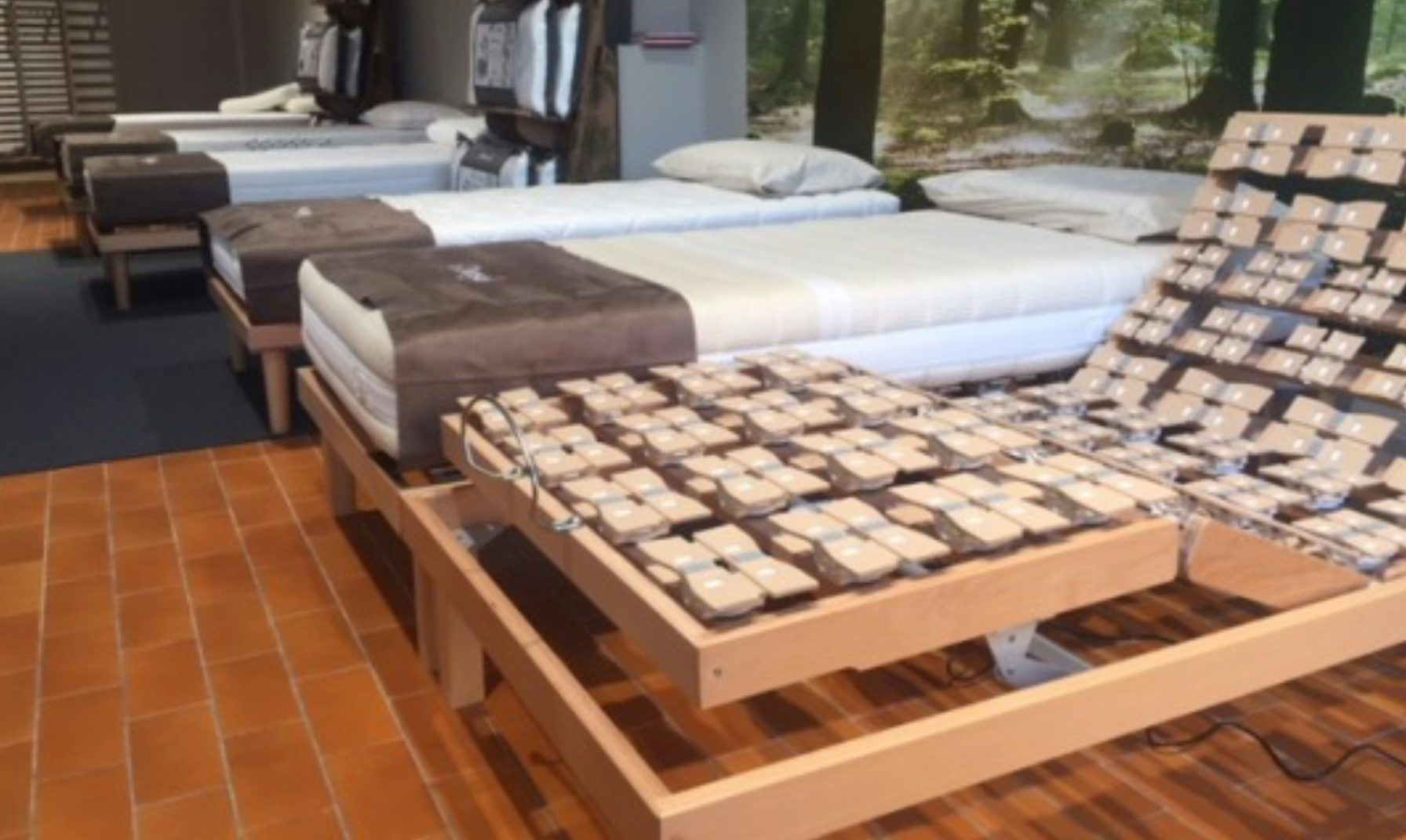 Letti singoli con rete regolabile e materassi in esposizione su pavimento in mattonelle arancioni in showroom.