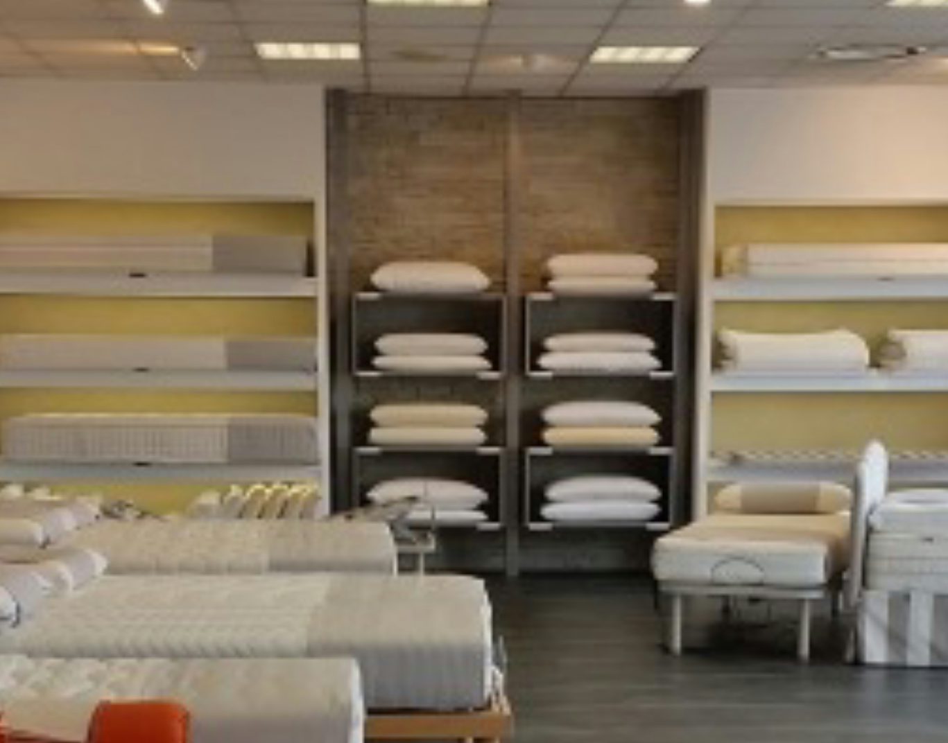 Negozio con letti matrimoniali e singoli, cuscini e reti esposti su scaffali e pavimento in legno scuro.