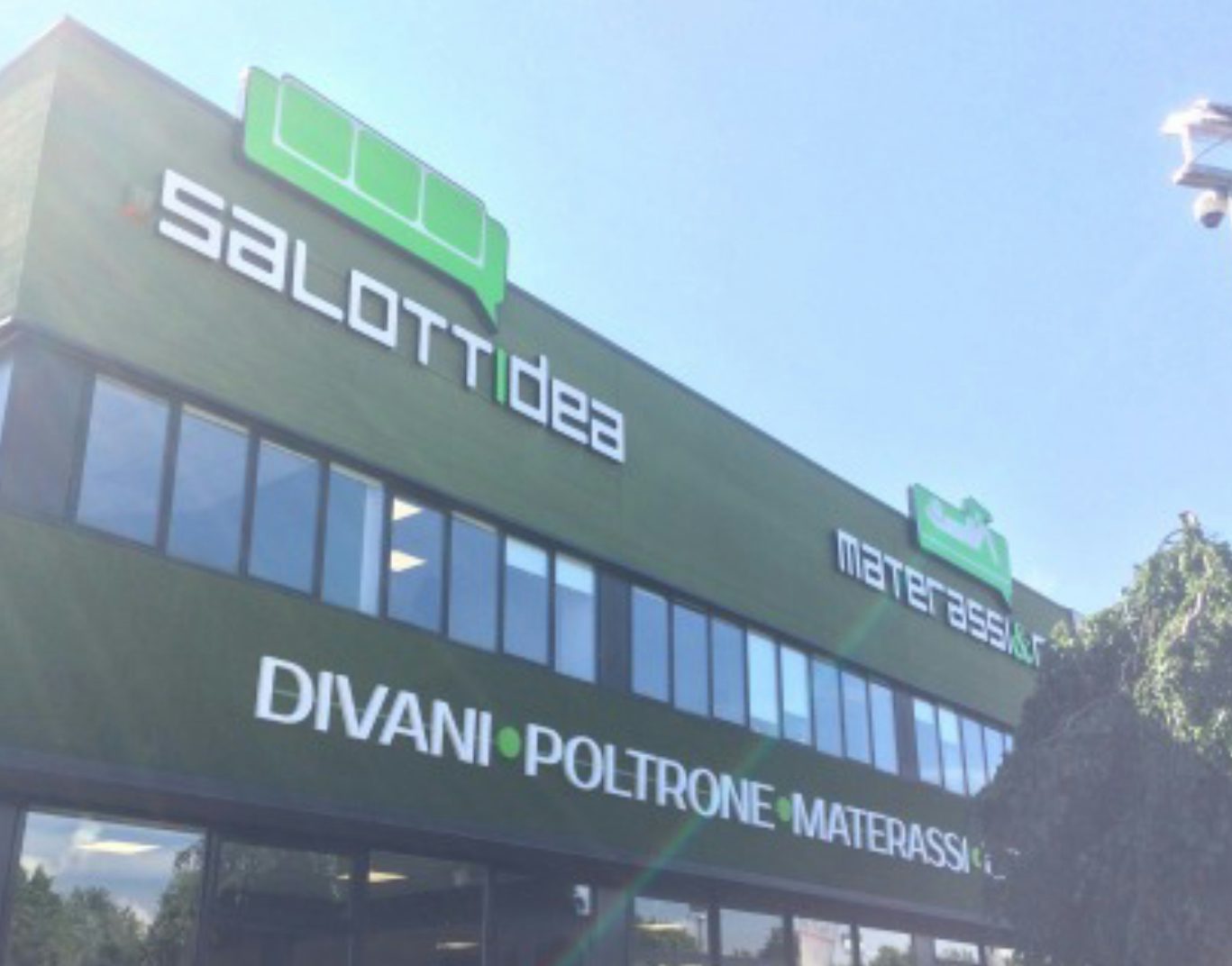Facciata verde scuro con insegne salotti idea, materassi & co, divani poltrone materassi sotto cielo azzurro.