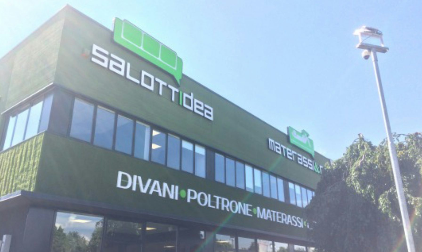 Facciata verde scuro con insegne salotti idea, materassi & co, divani poltrone materassi sotto cielo azzurro.