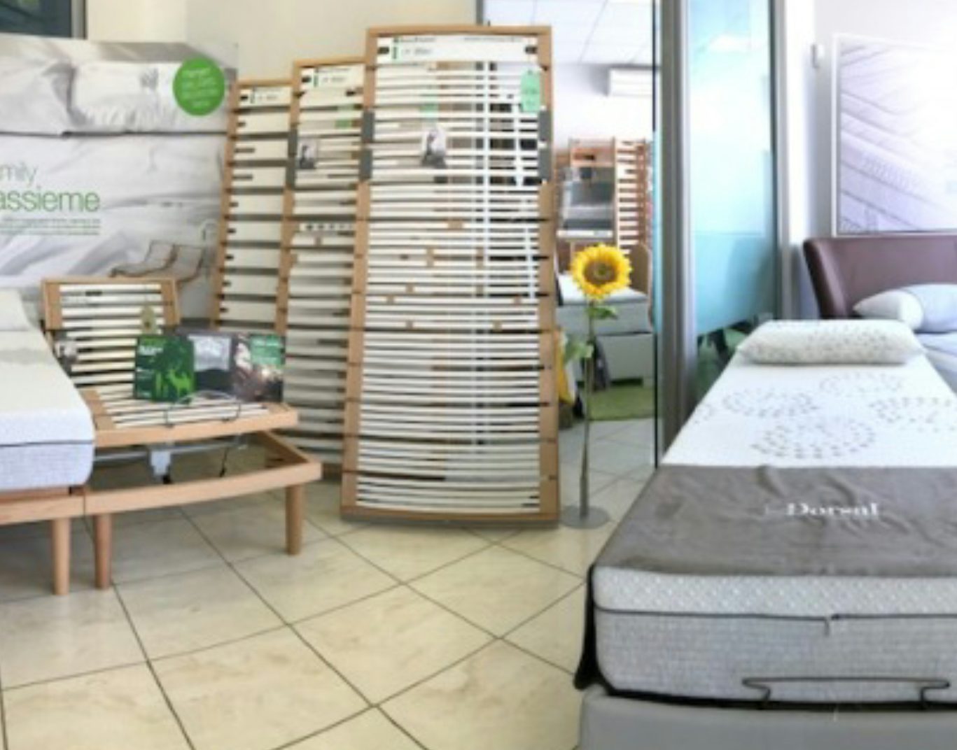 Showroom con letti matrimoniali, reti a doghe in legno e materassi con cuscini, pavimento piastrellato chiaro.