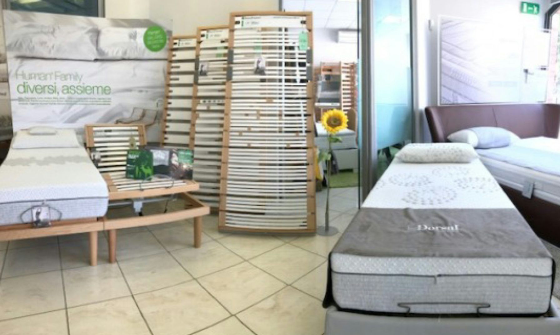 Showroom con letti matrimoniali, reti a doghe in legno e materassi con cuscini, pavimento piastrellato chiaro.