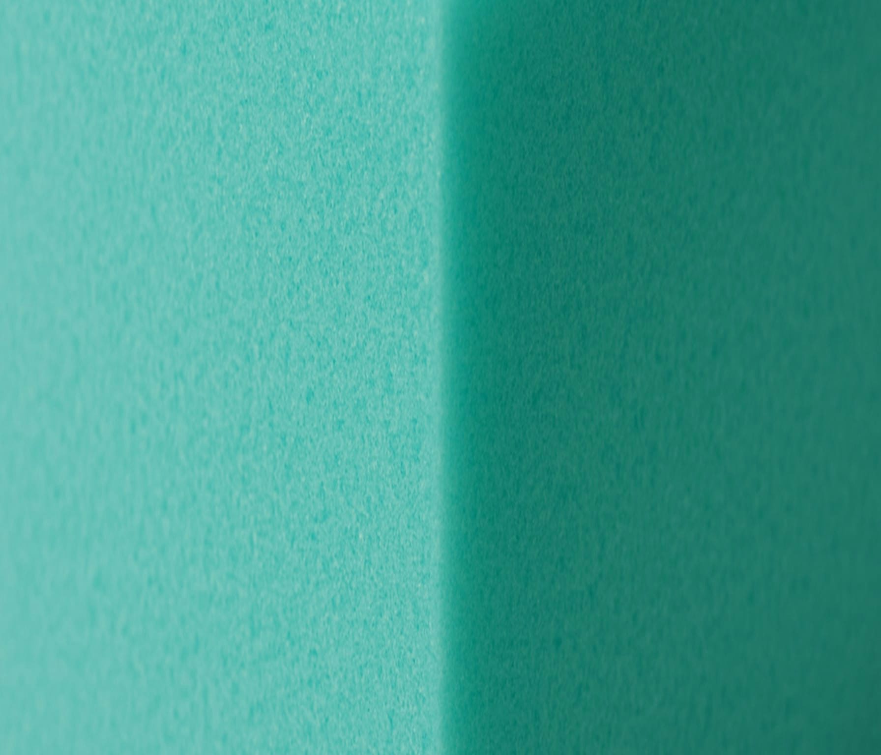 Superficie verde acqua con ombra verticale al centro che crea un contrasto di tonalità sul muro.