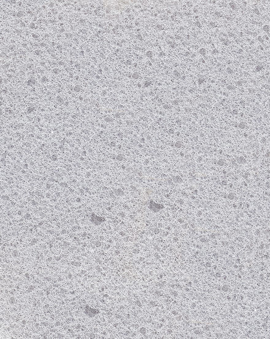 Superficie grigia con struttura granulosa e porosa, simile a un materiale lapideo o cemento grezzo.