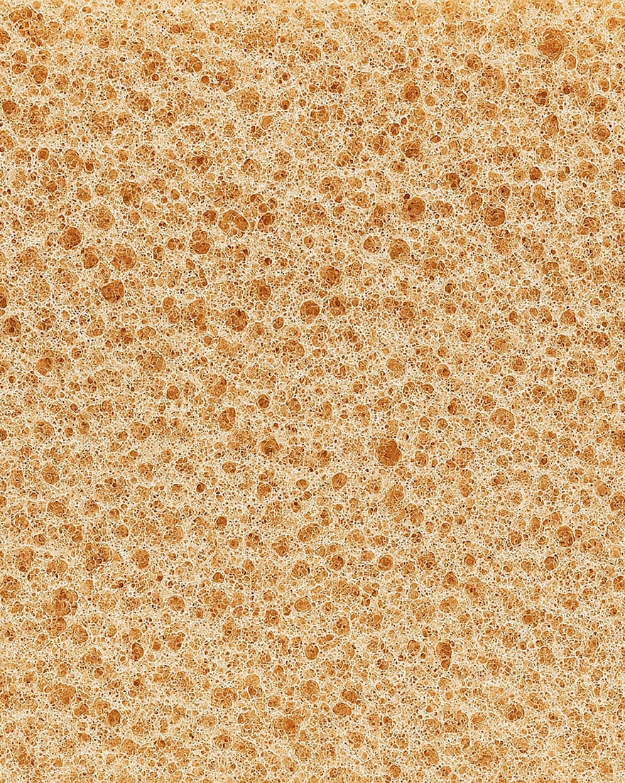 Superficie porosa di schiuma marrone chiaro con bolle di varie dimensioni distribuite uniformemente.