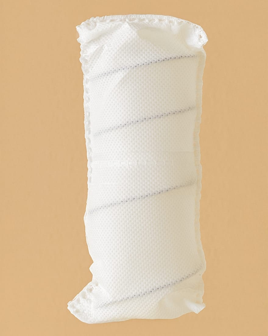 Cuscino anatomico bianco con fodera traspirante in tessuto a rete su sfondo beige.