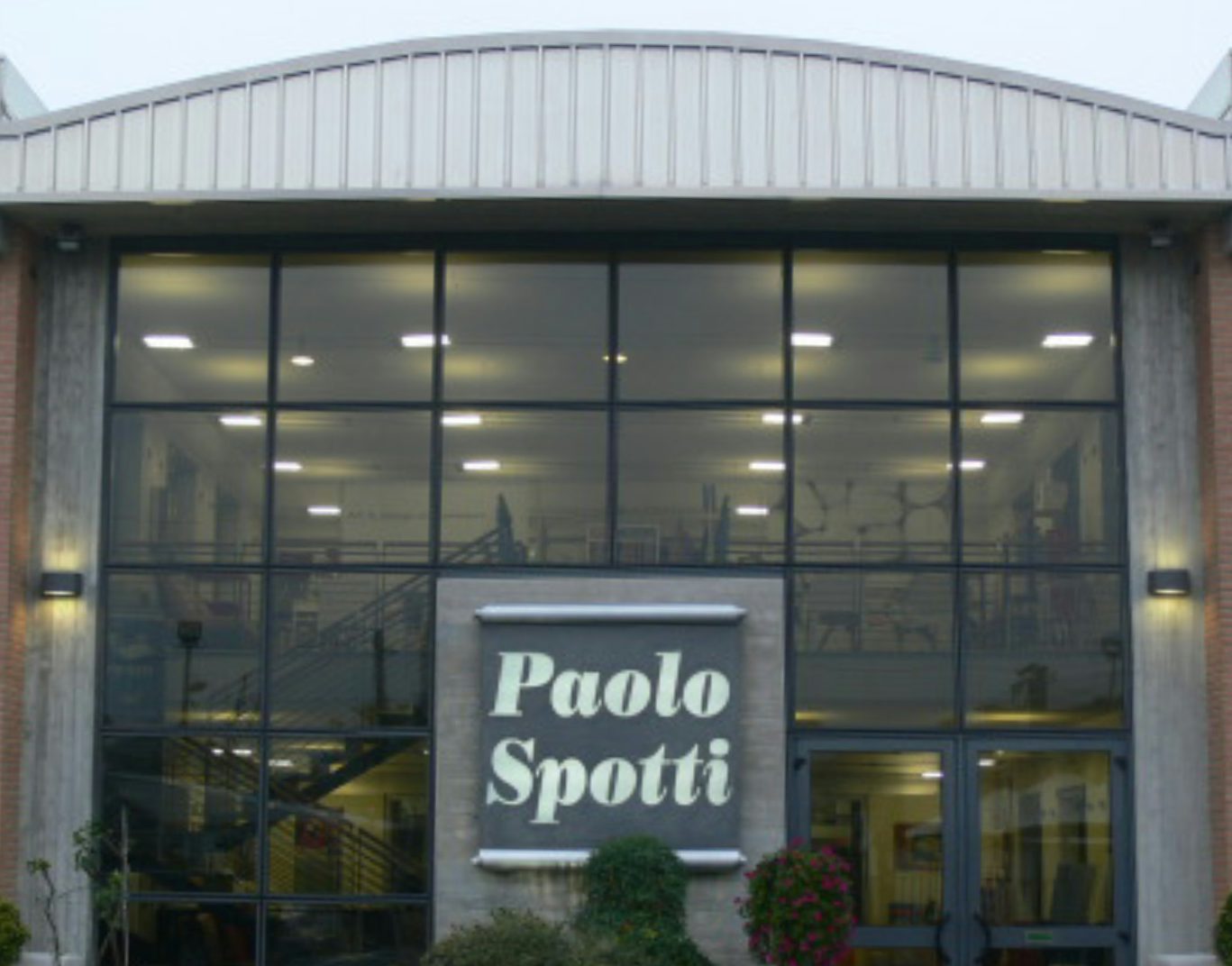 Facciata vetrata di edificio con insegna Paolo Spotti e piante davanti all'ingresso.