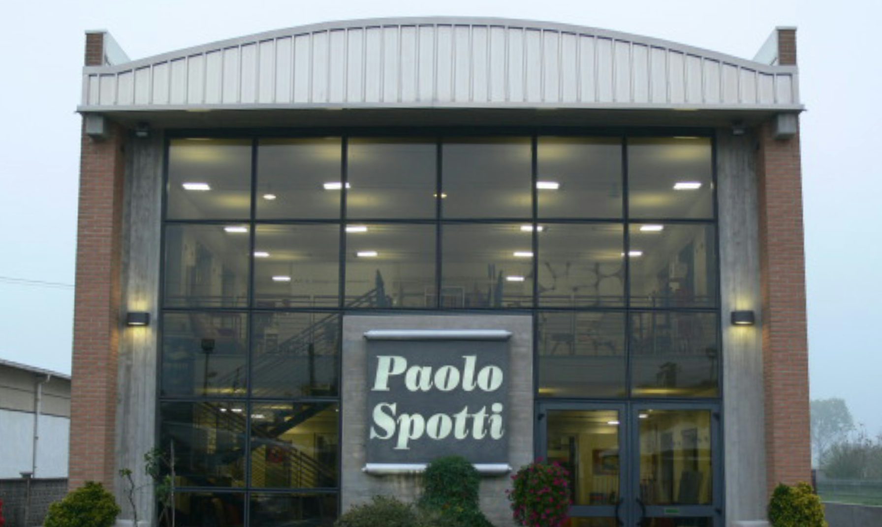 Facciata vetrata di edificio con insegna Paolo Spotti e piante davanti all'ingresso.