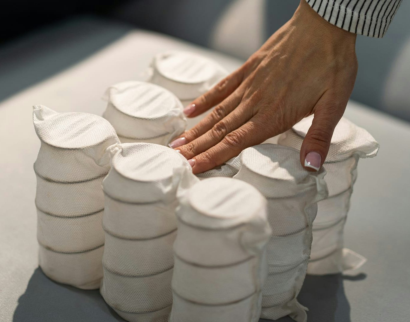 Mano che preme molle a cilindro avvolte in tessuto bianco su fondo grigio chiaro.