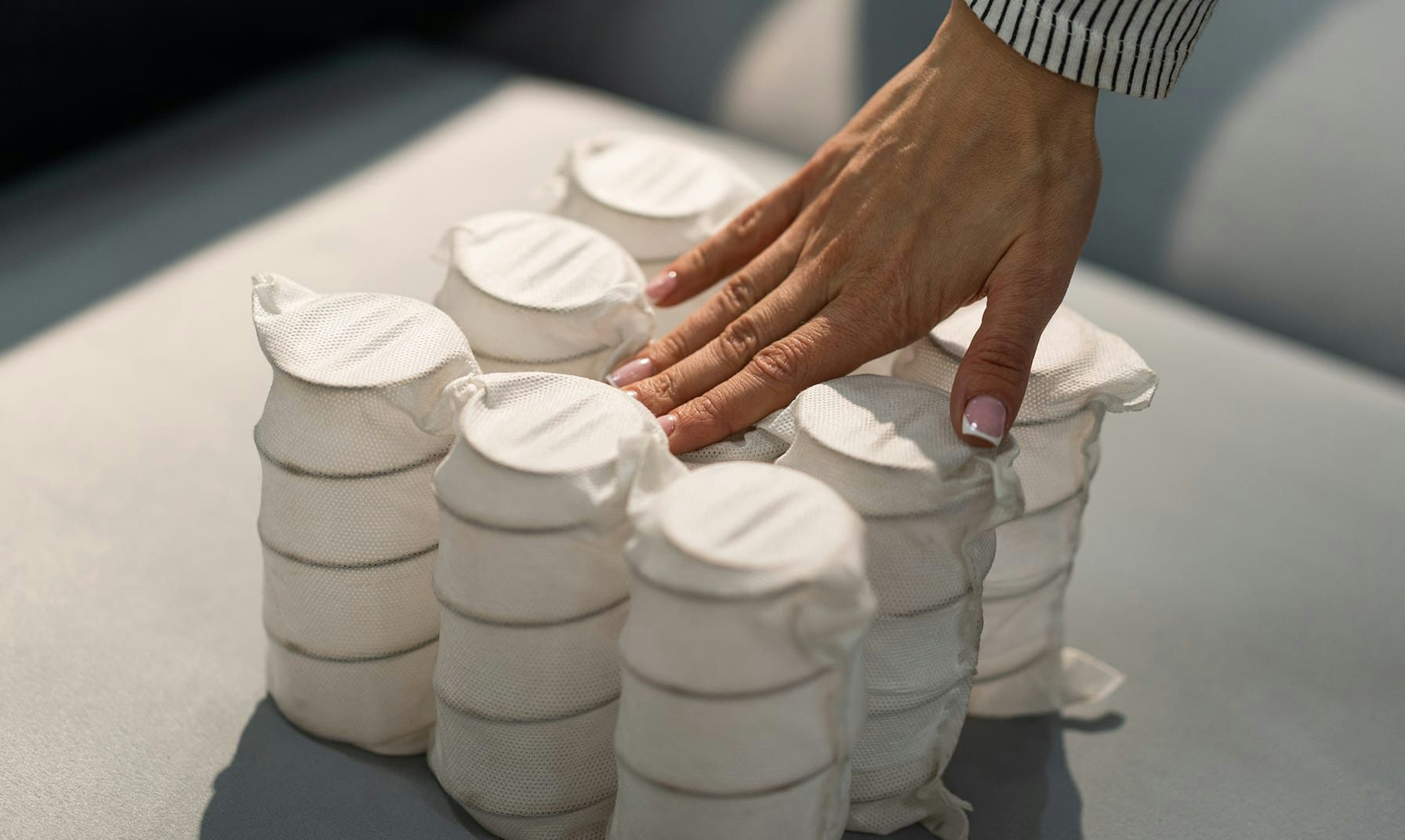 Mano che preme molle a cilindro avvolte in tessuto bianco su fondo grigio chiaro.
