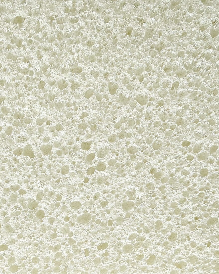 Superficie bianca con texture porosa irregolare simile a schiuma o spugna.