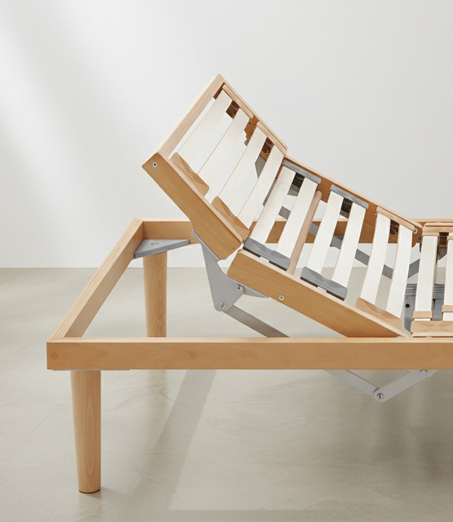 Base letto in legno chiaro con doghe sollevabili e supporto regolabile in acciaio grigio su pavimento cemento.