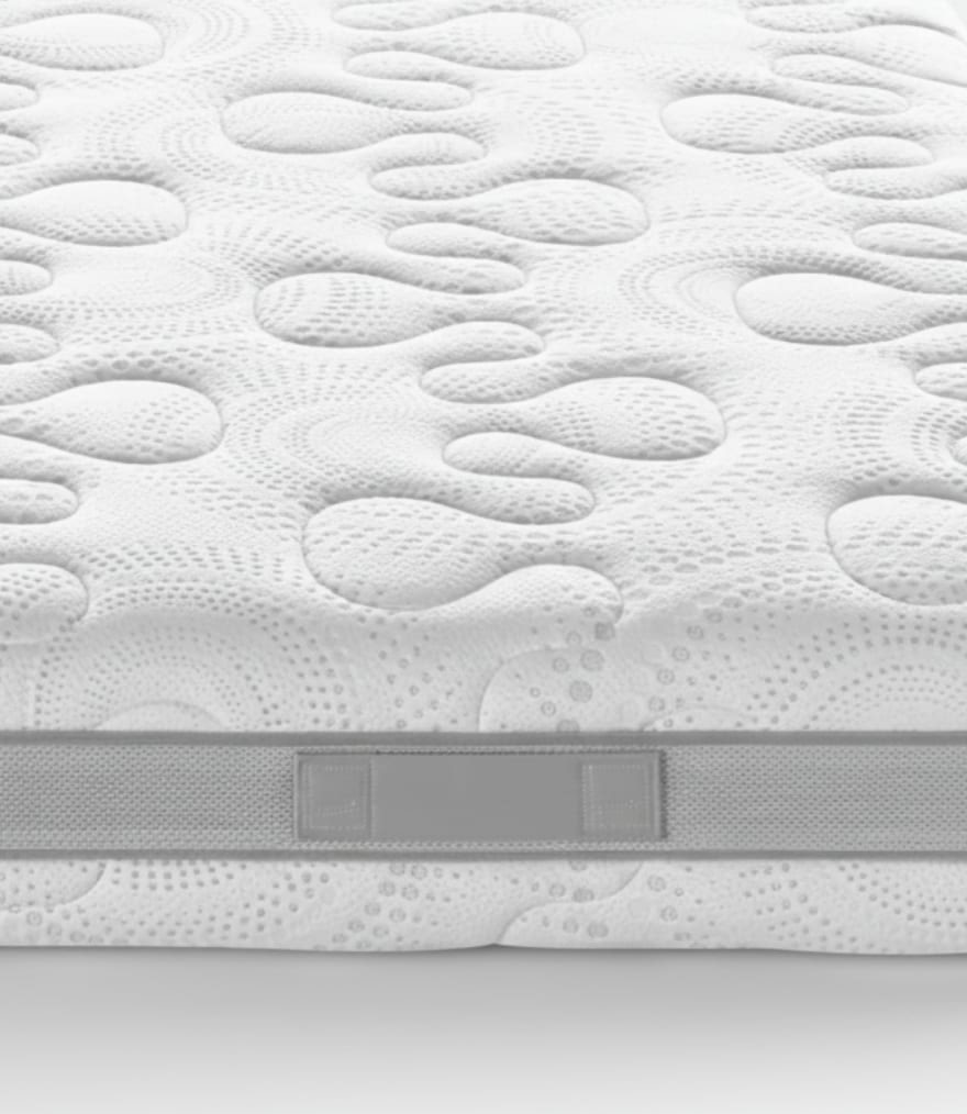 Particolare di materasso bianco con superficie trapuntata a bolle e maniglia grigia laterale.