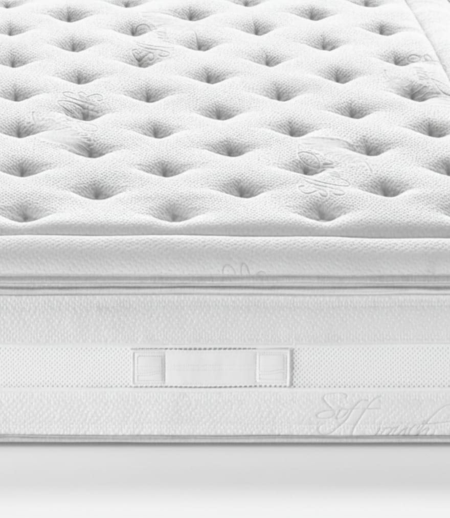 Materasso bianco con superficie trapuntata, maniglione laterale e dettagli ricamati effetto soffice.